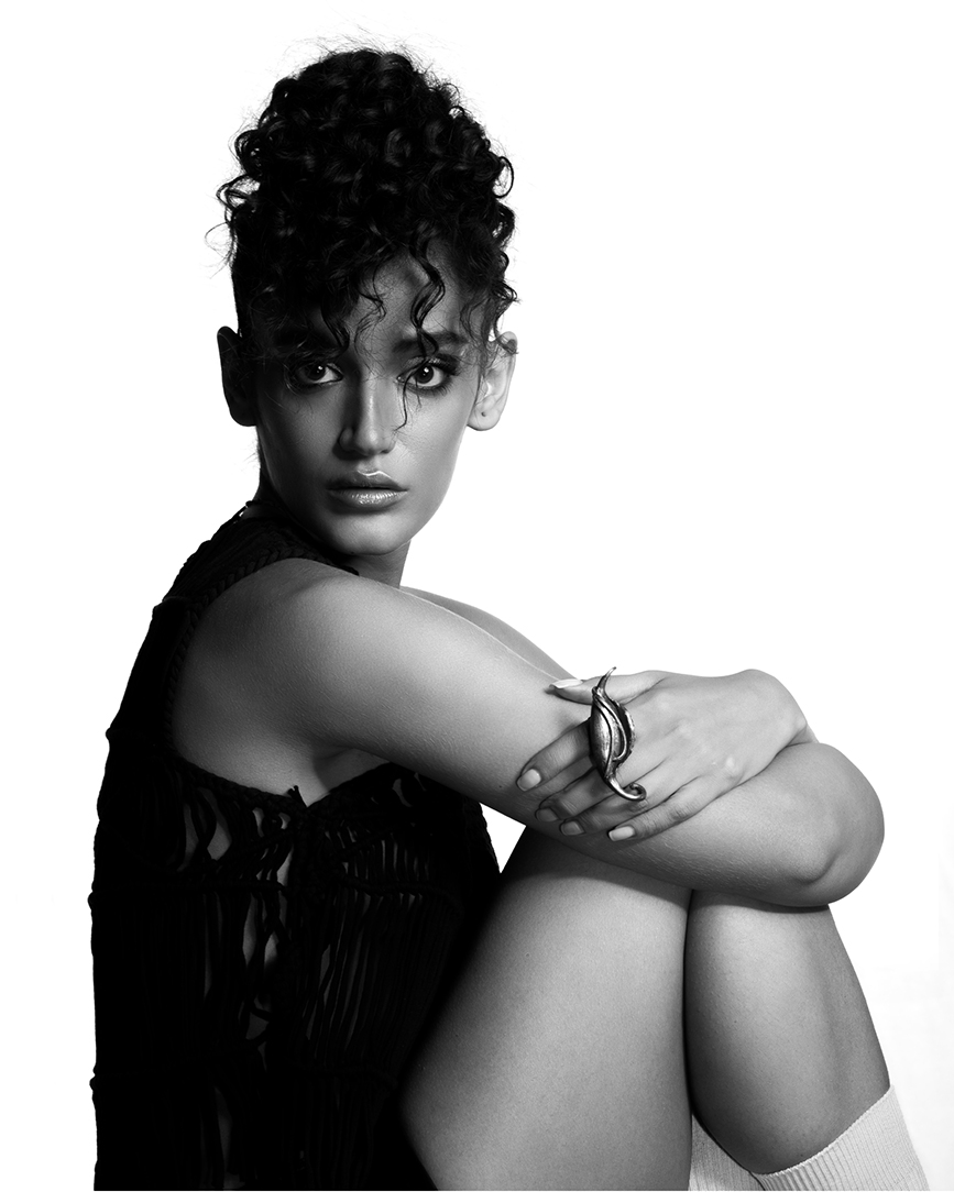 Black and white editorial portrait of a model seated with her arms around her knees