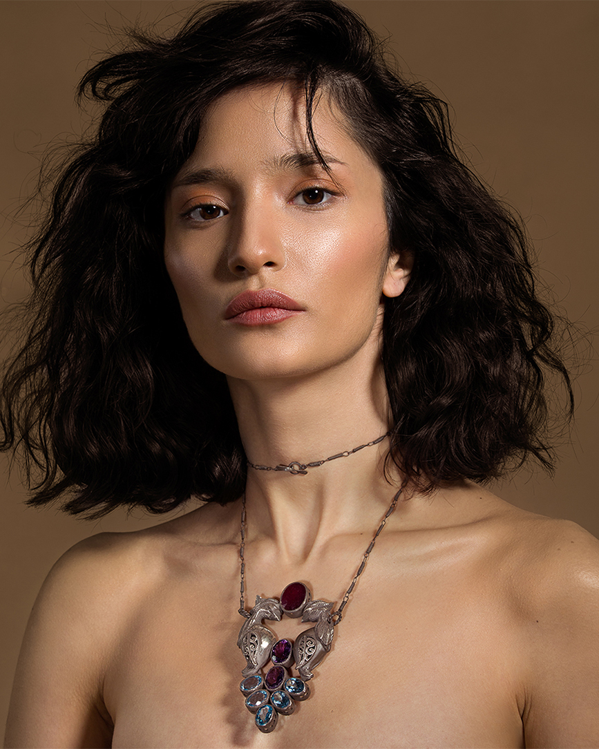 Editorial portrait of a model with dark wavy hair wearing layered pendant necklaces