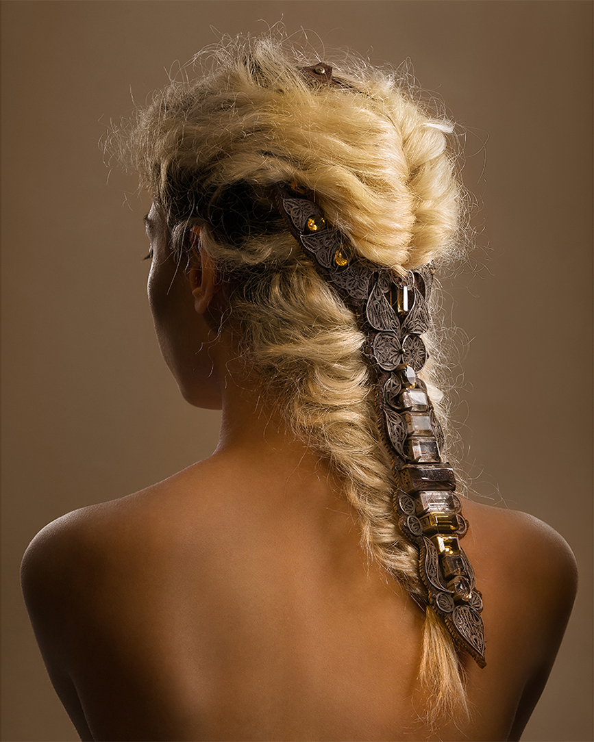 Back view of a model with a blond braided hairstyle decorated with metal jewelry