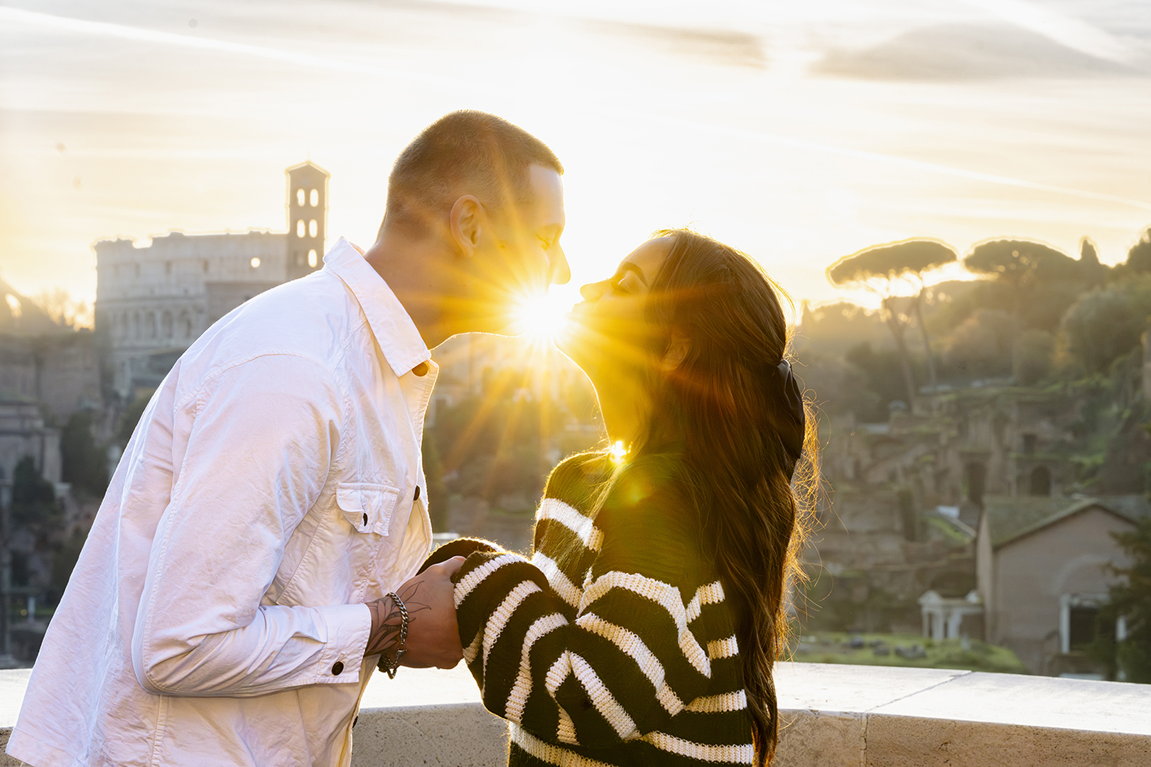 Backlit kiss at sunset on Capitoline Hill with sun flare and the Roman Forum skyline.