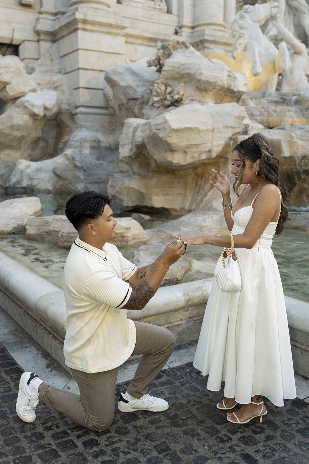 Surprise proposal at Trevi Fountain Rome, groom putting engagement ring on fiancée's hand