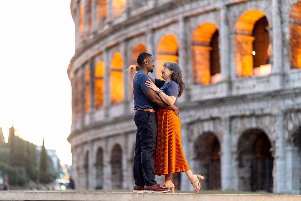 Couple seated together near the illuminated Colosseum, surrounded by golden arches and a deep blue sky — cinematic Blue Hour photoshoot by Rome photographer Jeff.