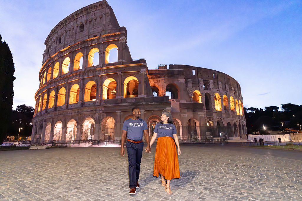 Couple walking hand in hand in front of the illuminated Colosseum during Blue Hour, captured by Eidos Photography — Rome photographer specializing in cinematic early-morning shoots.
