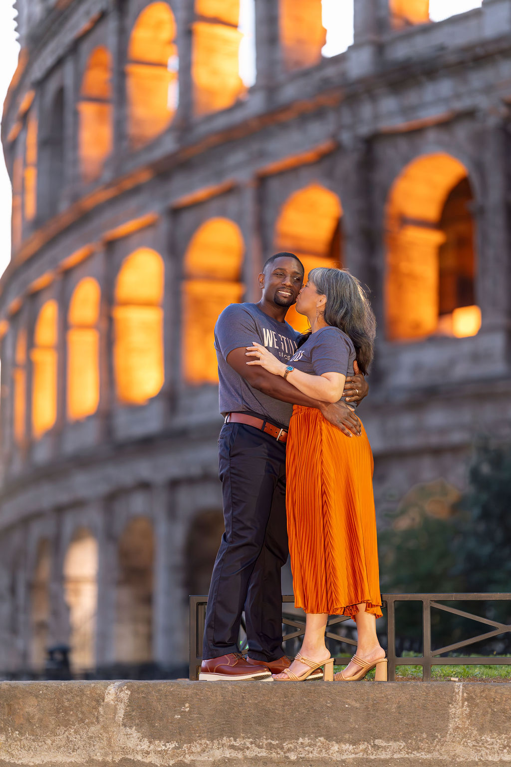 Woman framed beneath the glowing Colosseum arch at Blue Hour, warm orange light contrasting the deep blue sky — editorial photoshoot in Rome by Eidos Photography.