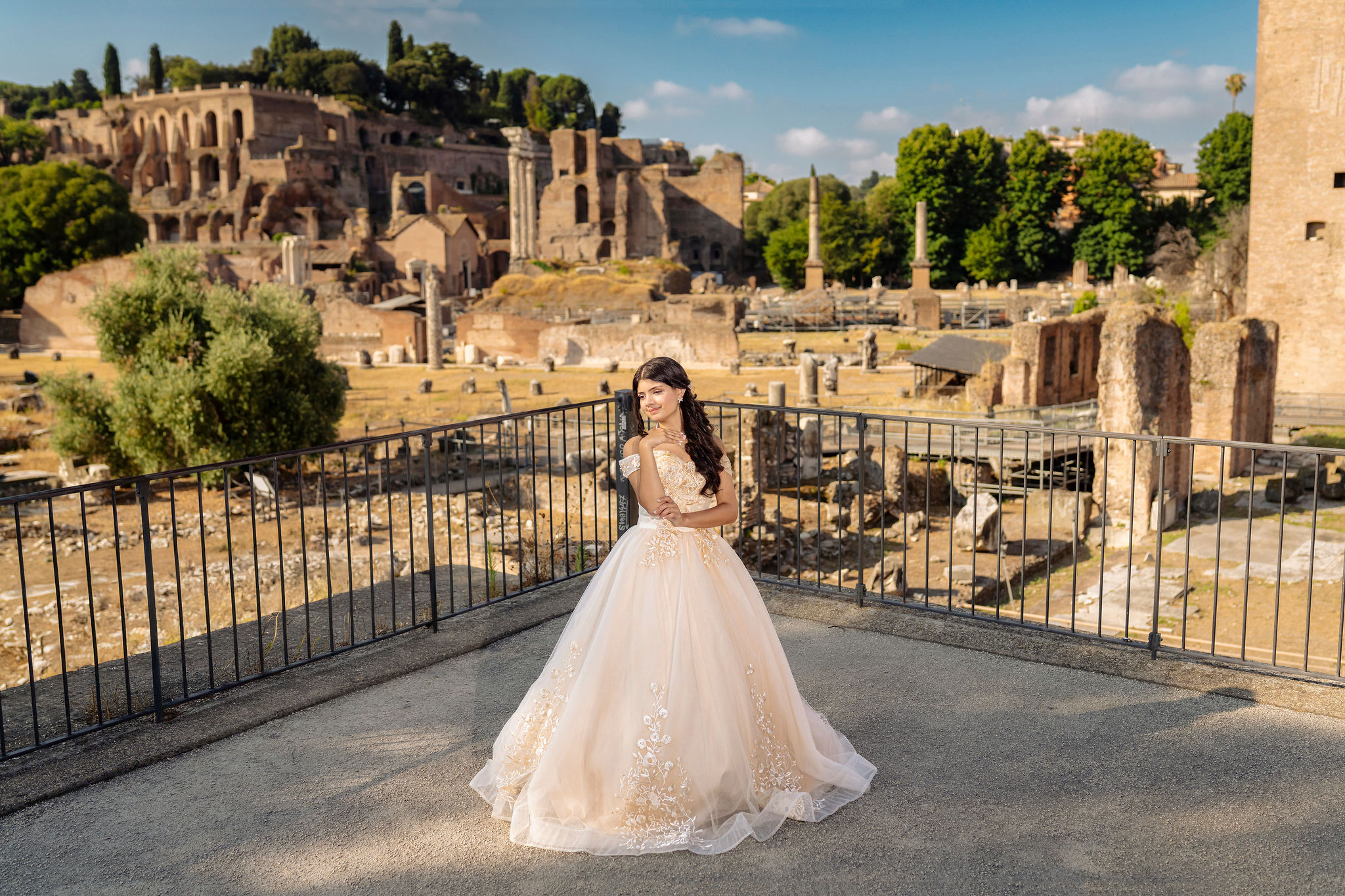 quinceañera in an ivory ball gown on a terrace overlooking the Roman Forum ruins near the Colosseum at first light in Rome