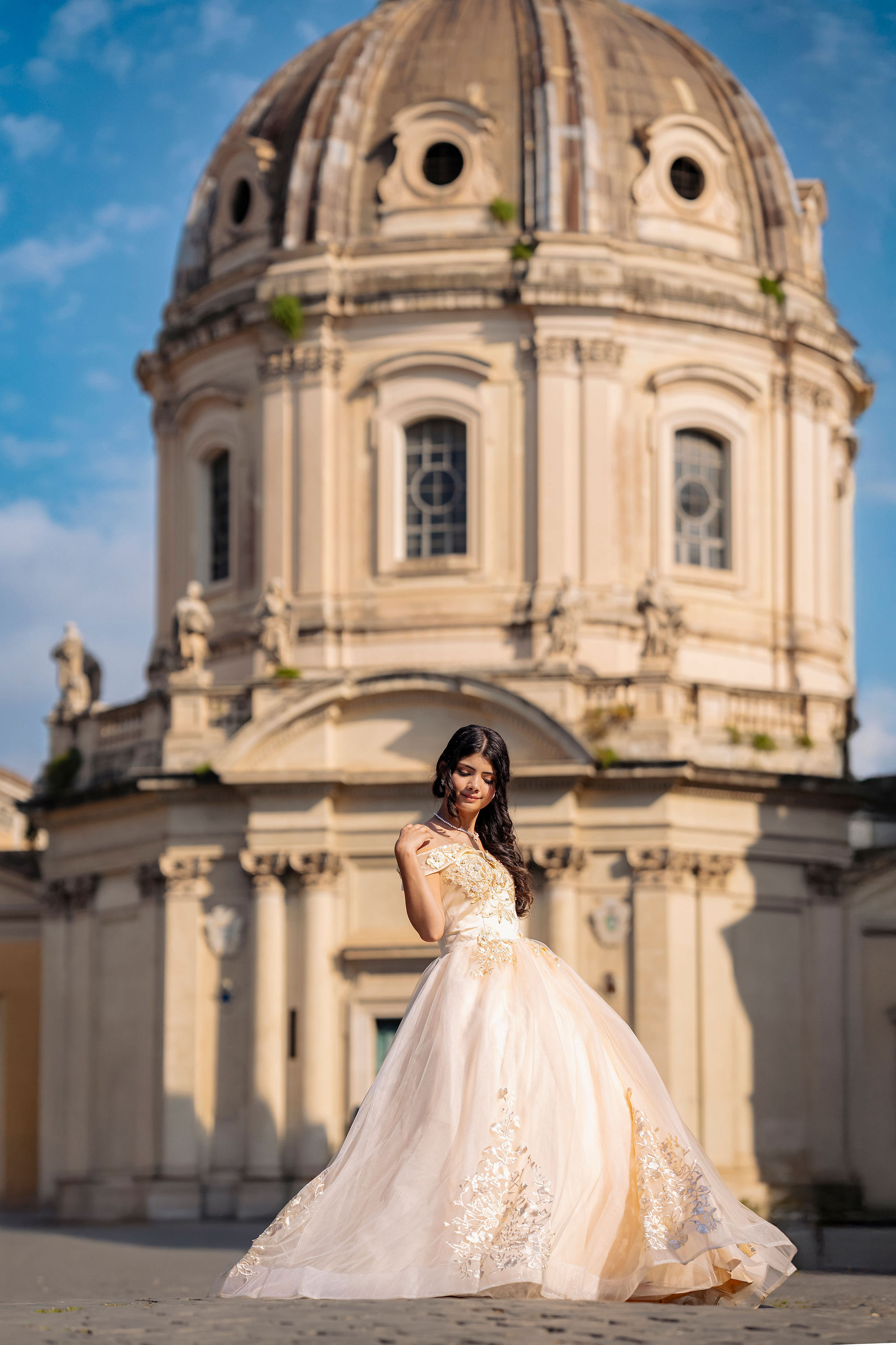 portrait of a quinceañera in an ivory off-shoulder ball gown with a Baroque church dome near the Roman Forum at first light in Rome