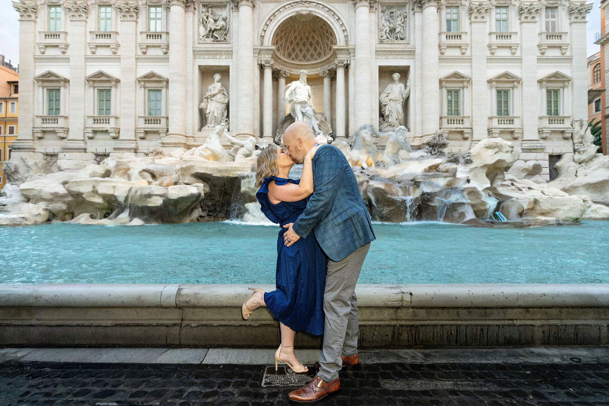 Couple kissing in front of the Trevi Fountain during an early morning Rome photoshoot, after a professional hair and makeup session.