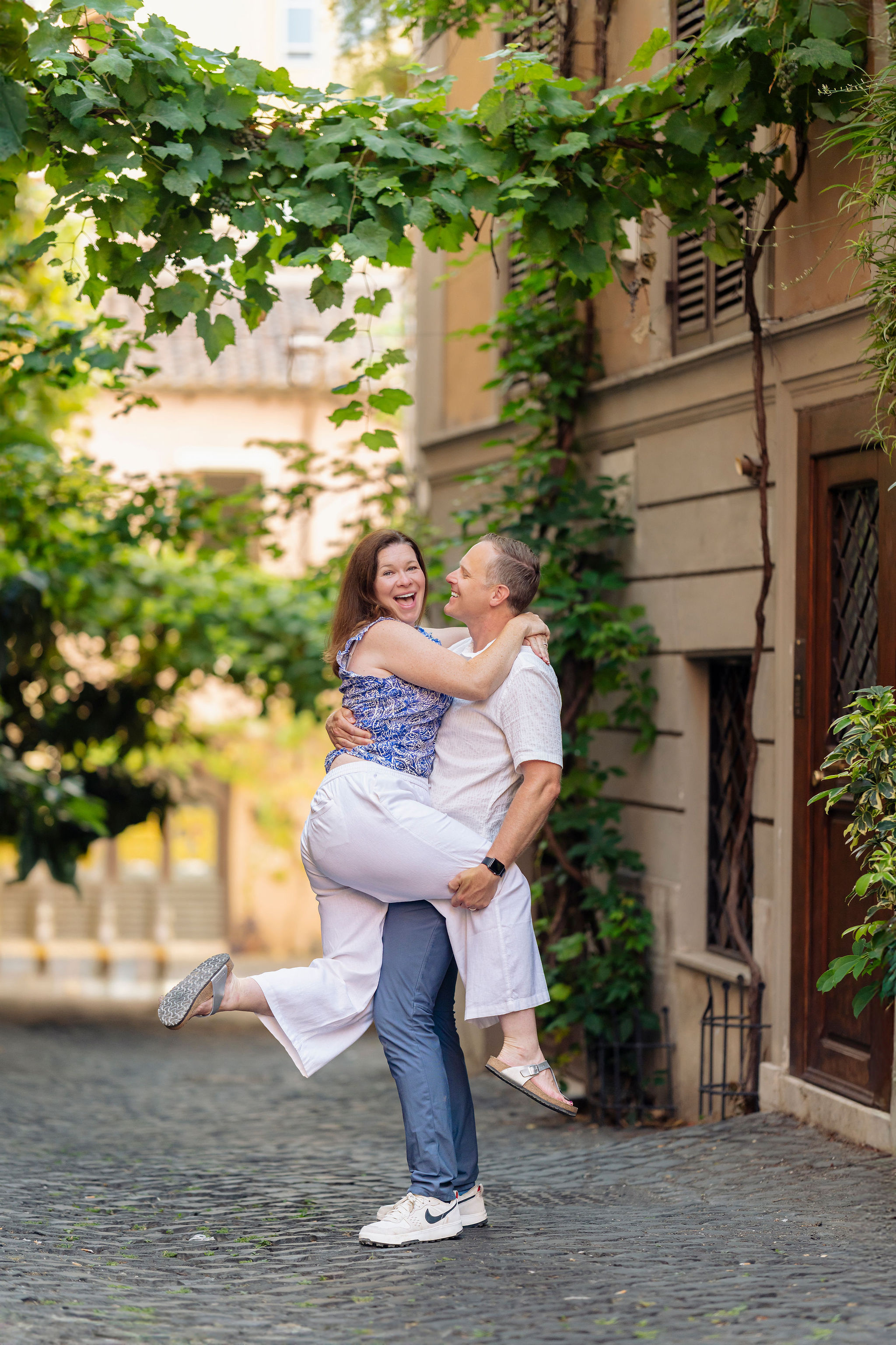 Husband lifting wife on a cobblestone lane in Monti, Rome during a family photoshoot by Eidos Photography, Rome photographer