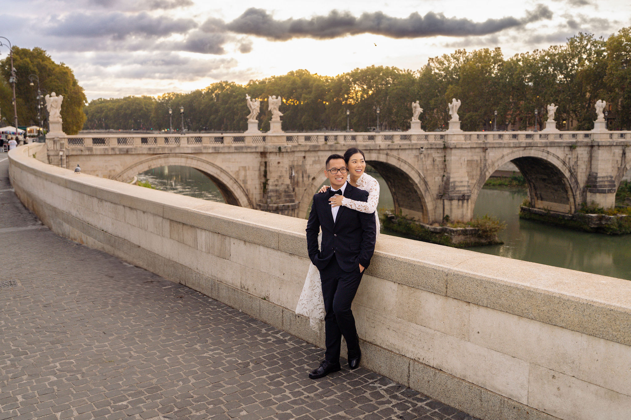 Couple standing on Ponte Sant’Angelo near Castel Sant’Angelo during blue hour in Rome, photographed by Eidos Photography, Rome photographer.