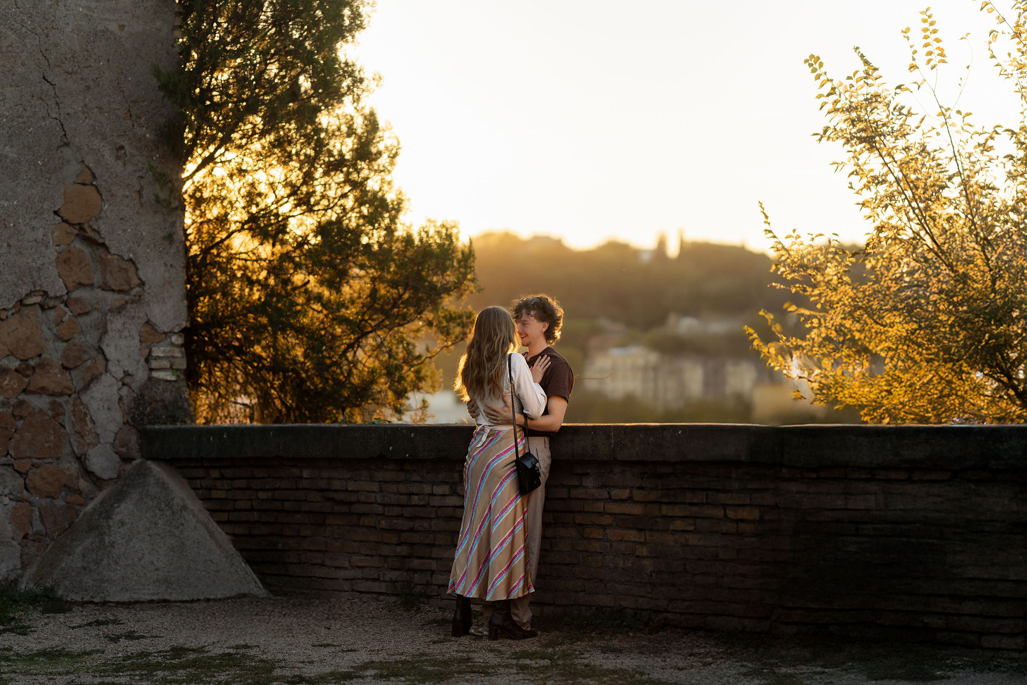 Wide cinematic sunset photo of a couple embracing on Aventine Hill in Rome during a secret proposal photoshoot, captured by Eidos Photography Rome photographer
