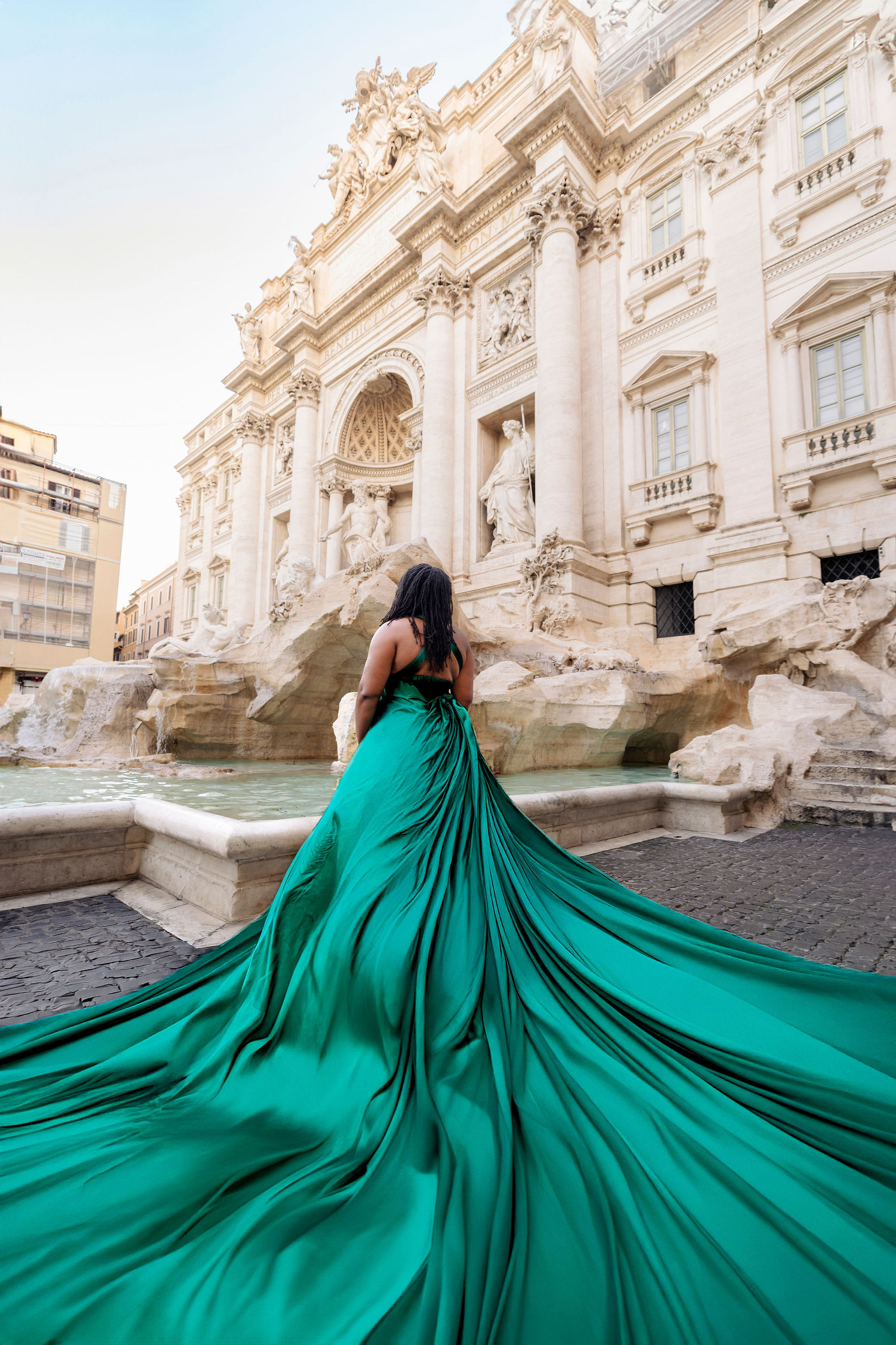      Woman in emerald flying dress with dramatic flowing fabric during an early morning flying dress photoshoot at Trevi Fountain in Rome by Eidos Photography, Rome photographer.