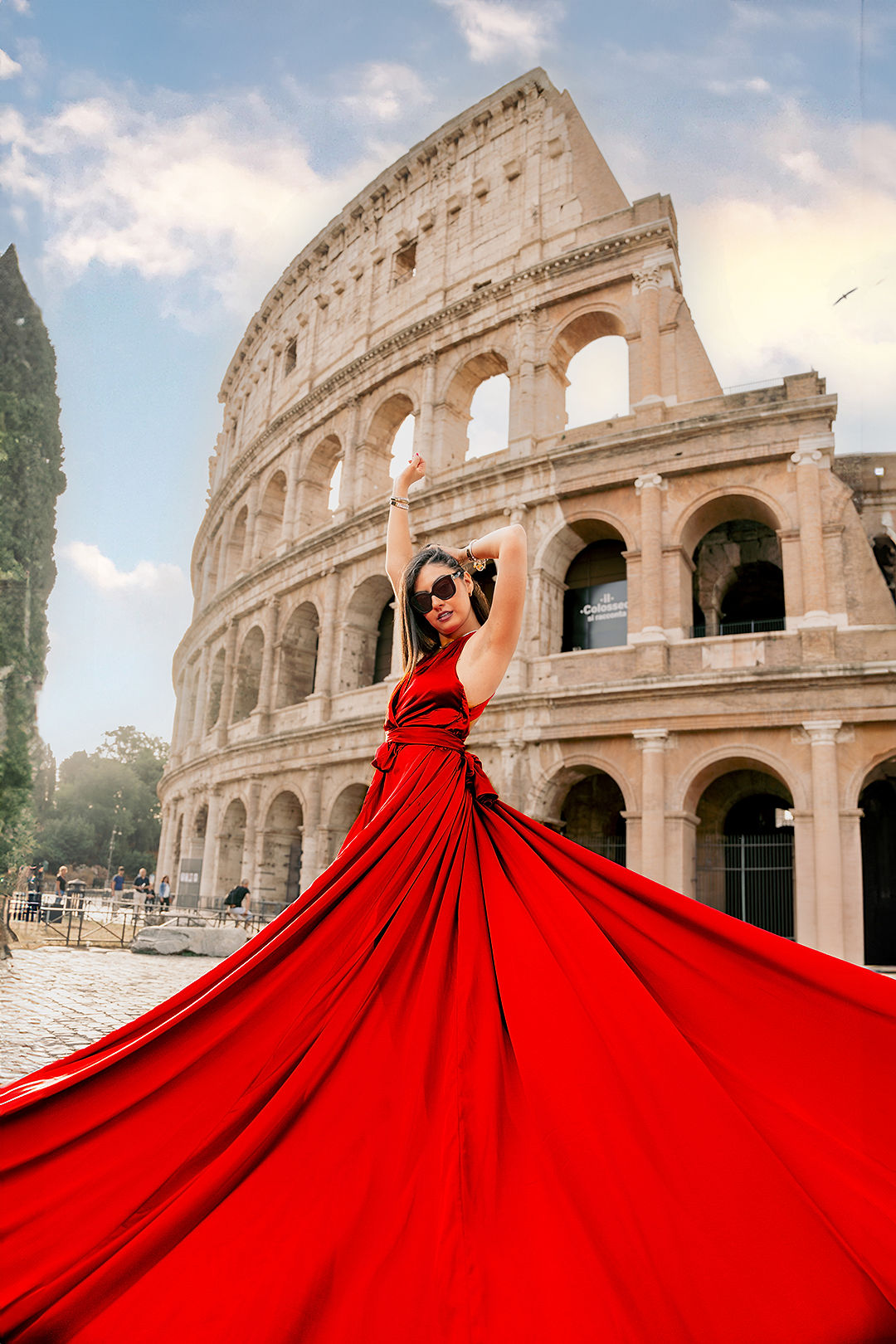 Woman in a dramatic red flying dress with flowing fabric in the foreground during a Colosseum flying dress photoshoot in Rome by Eidos Photography, Rome photographer.