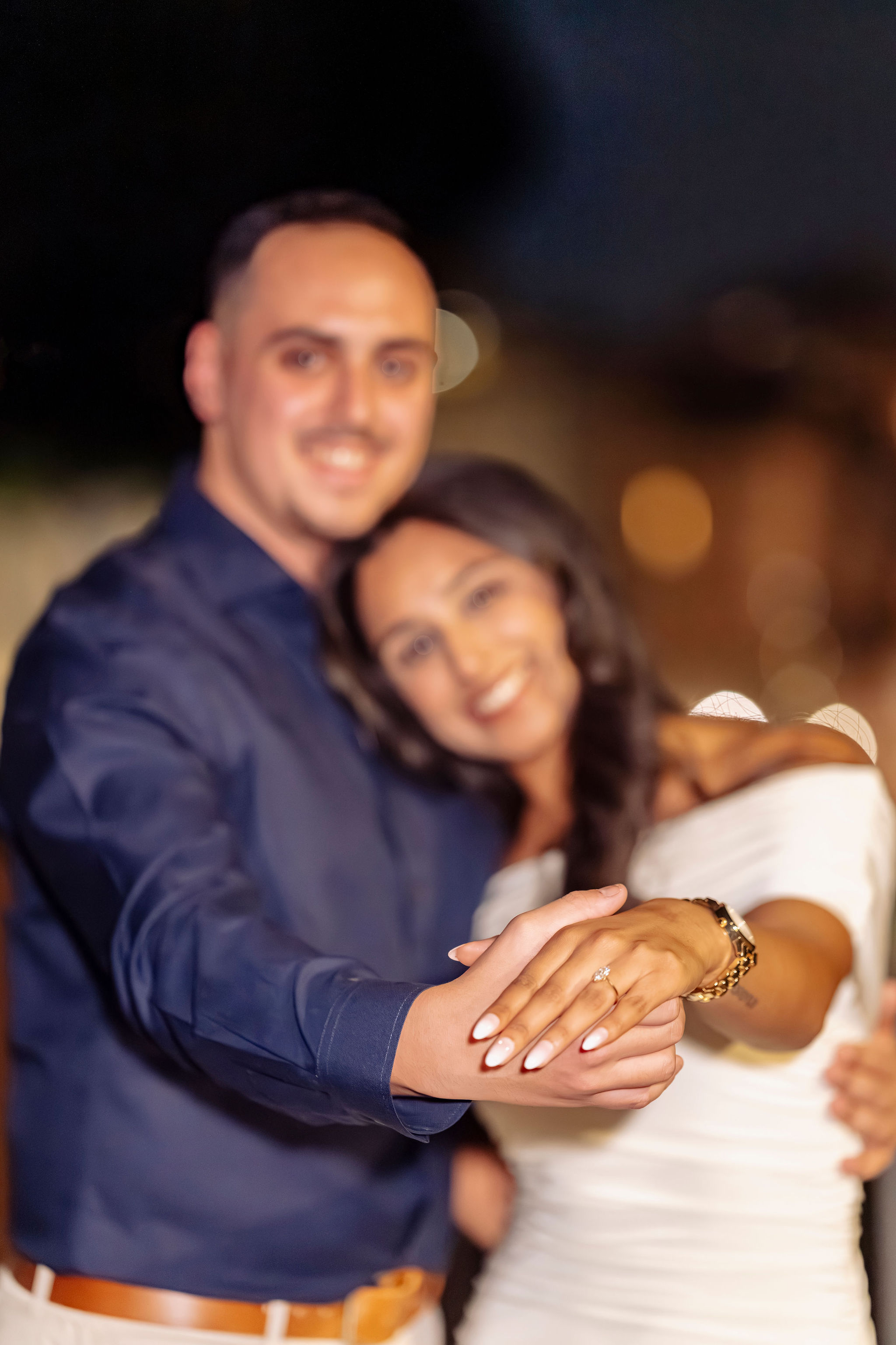 Close up engagement photo at night in Rome. Couple smiling in soft bokeh background while the woman holds out her hand showing the engagement ring. Secret proposal couple photoshoot by Eidos Photography, Rome photographer.
