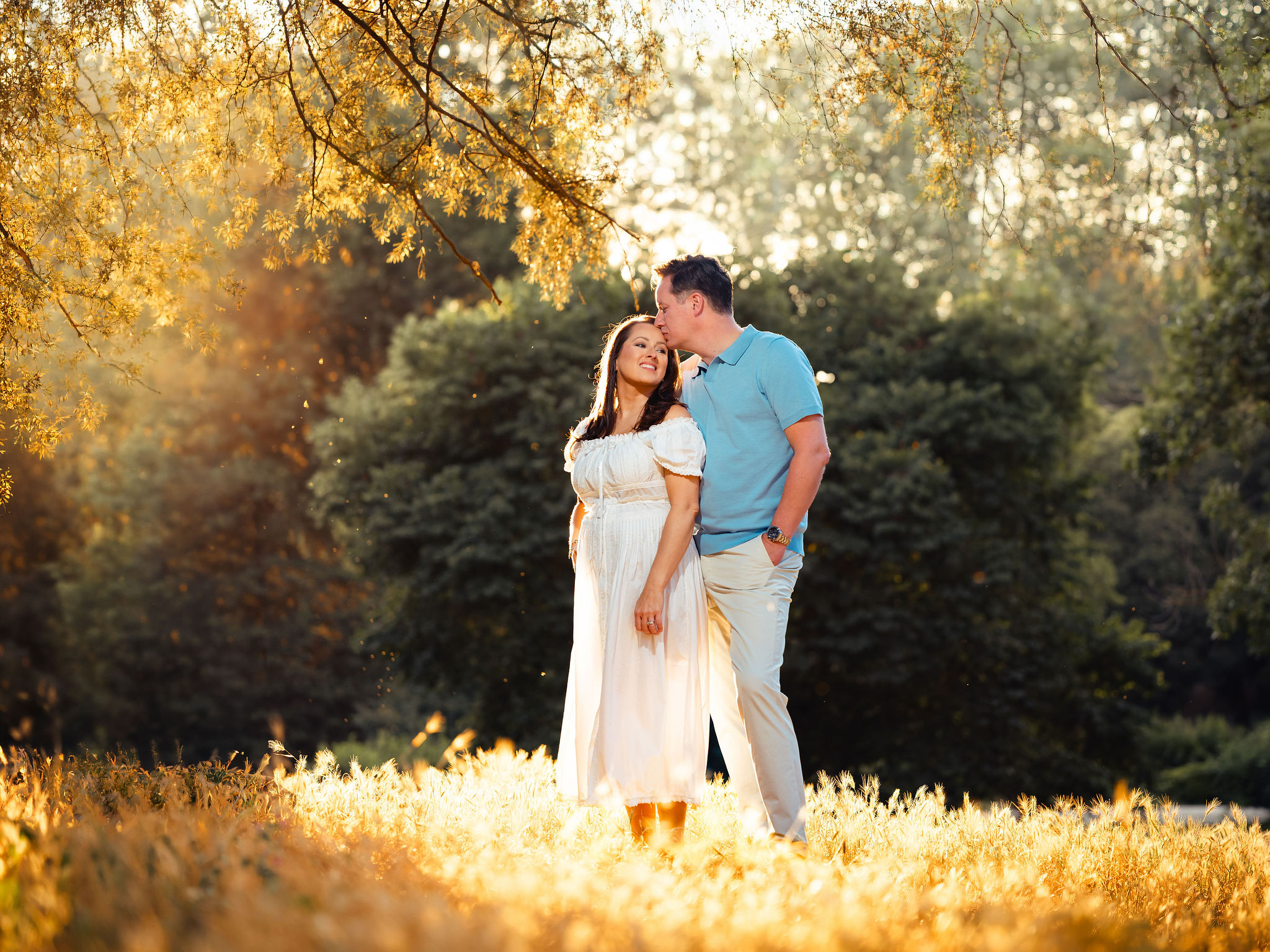 Couple posing during a sunset maternity photoshoot in a Rome garden, with golden light, green trees, and a romantic outdoor atmosphere captured by Eidos Photography.
