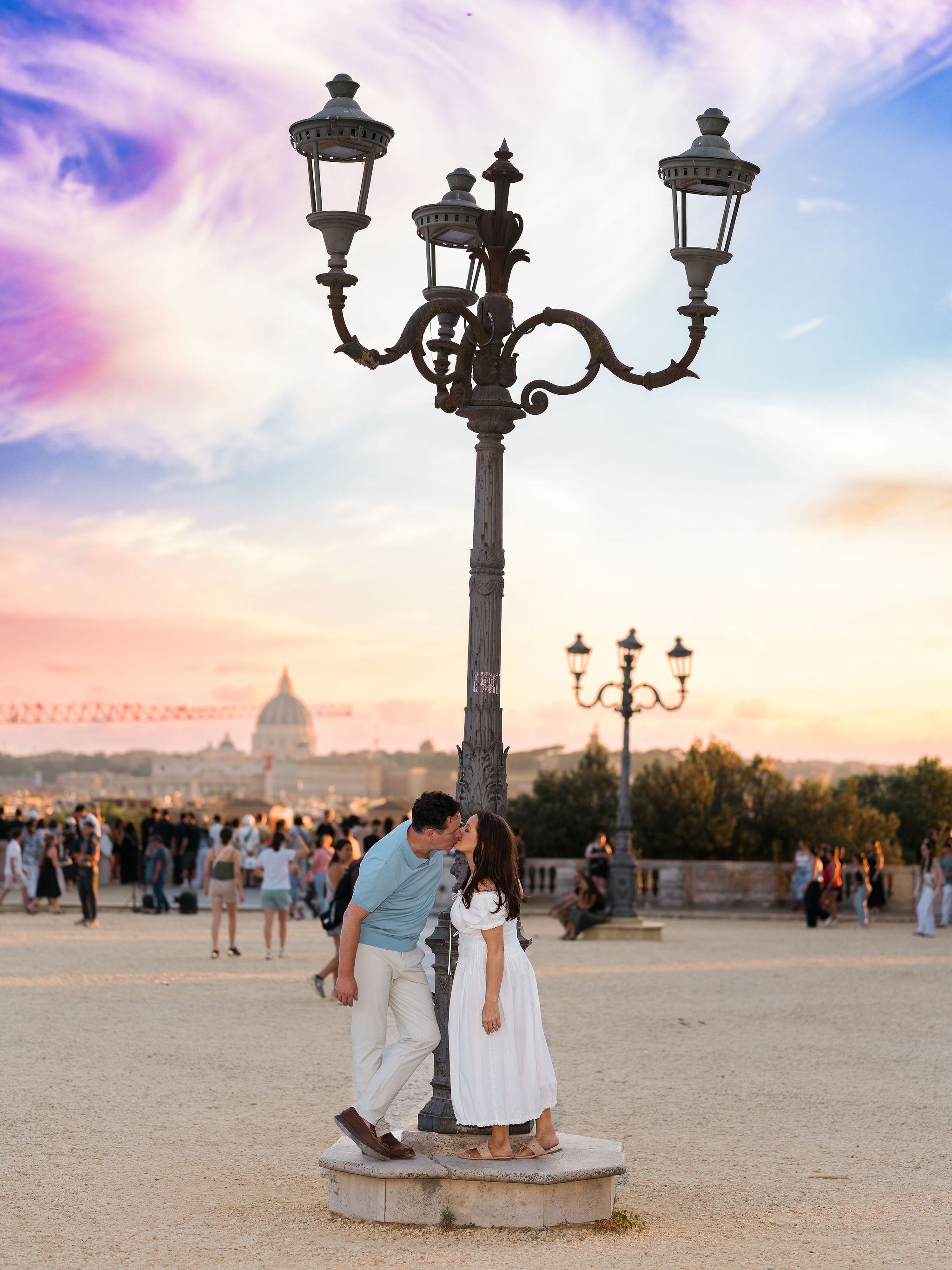 Couple sharing a kiss at Pincio Terrace in Villa Borghese during sunset, with St. Peter’s Basilica in the background and the warm evening light illuminating a romantic Rome photoshoot by Eidos Photography.