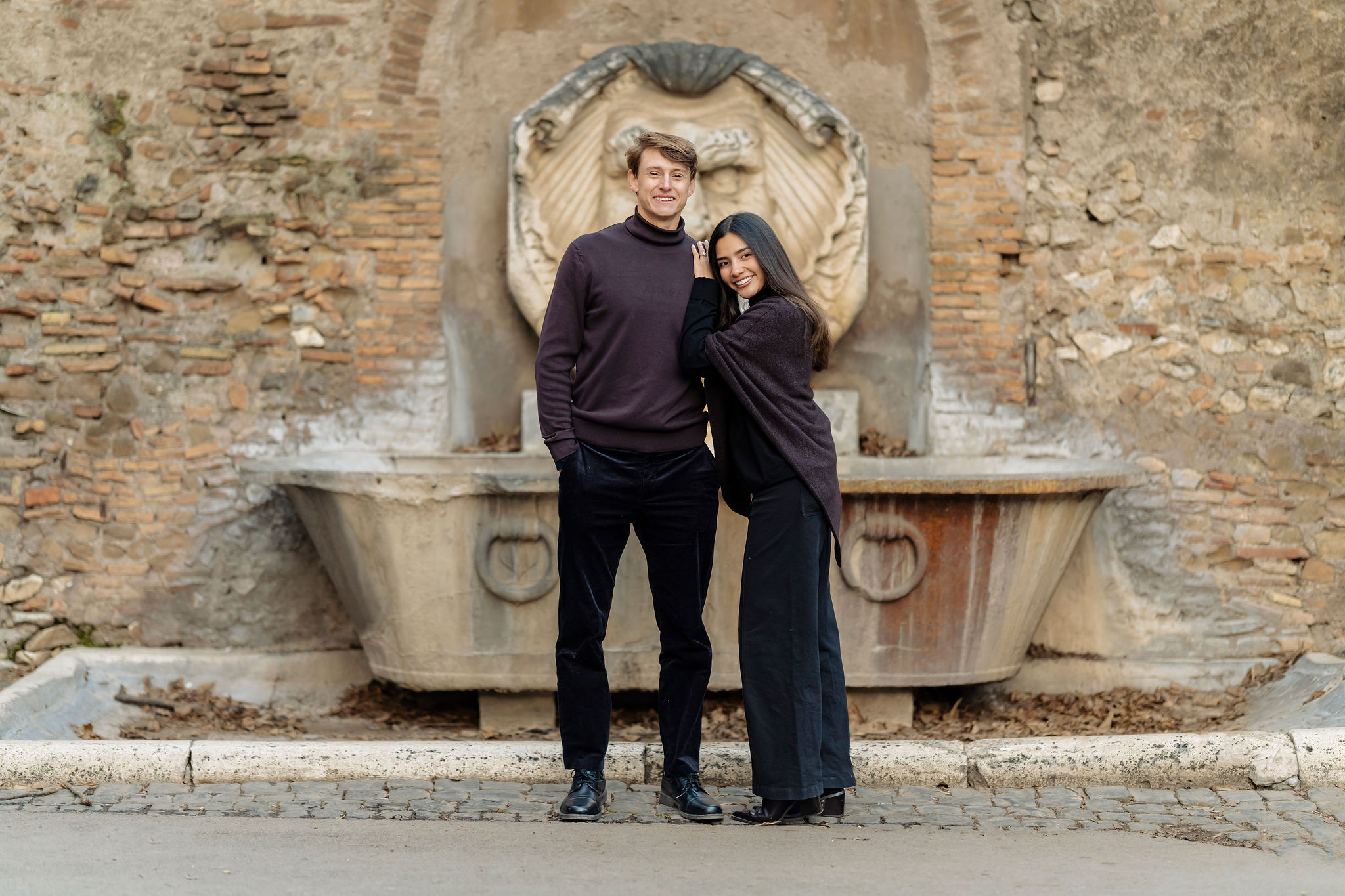 Couple posing in front of a historic stone fountain in Rome during a private photoshoot. The elegant architectural backdrop and soft natural light create a timeless, romantic portrait by Eidos Photography.