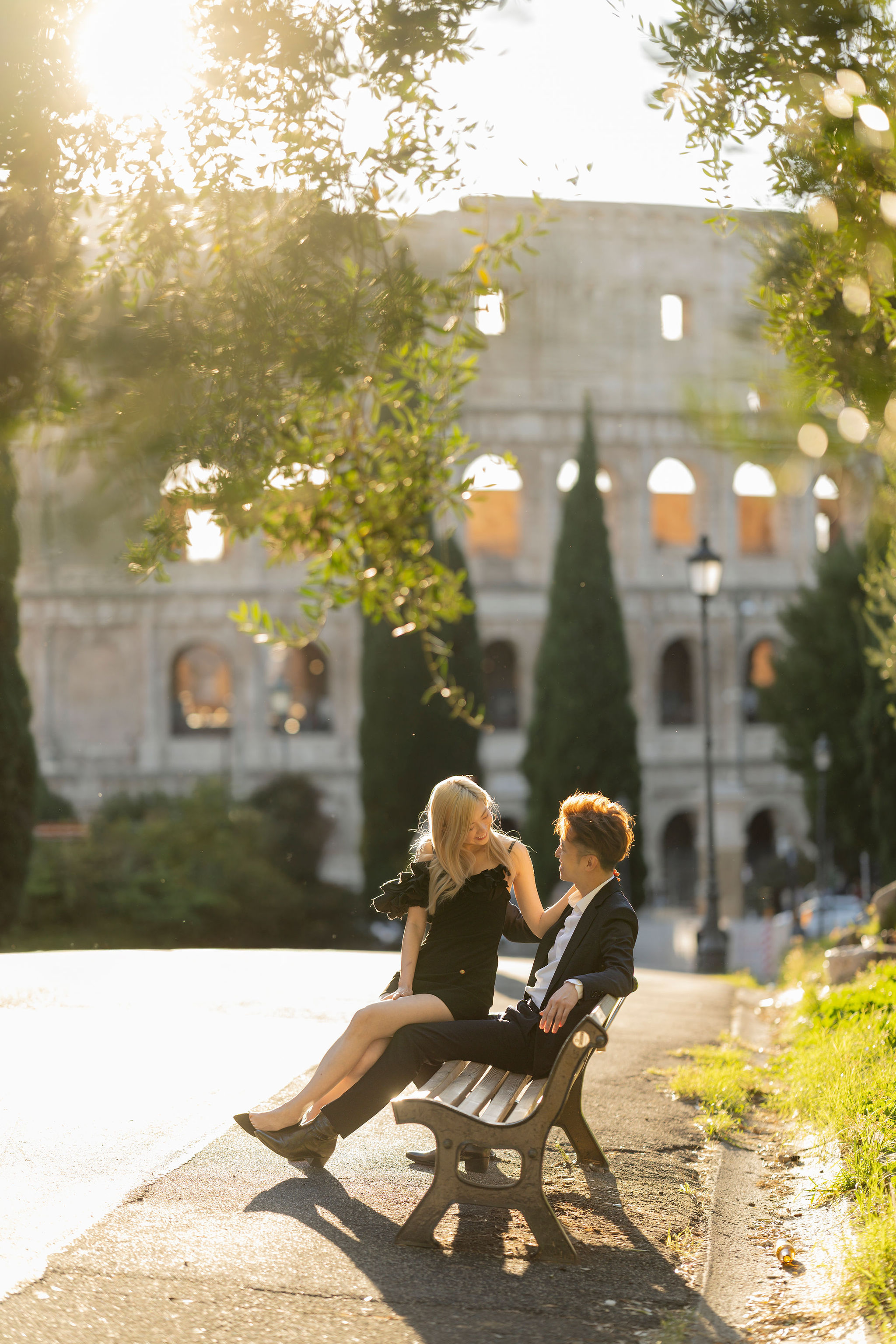 Couple posing among the cypress trees of Parco del Colle Oppio, with the Colosseum glowing in the background at sunset.