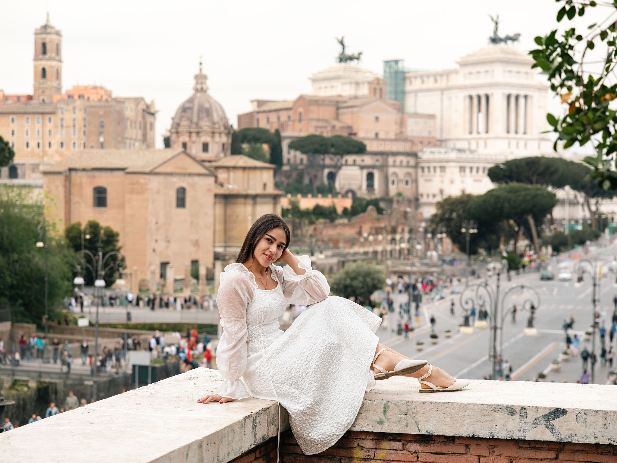 Woman in a flowing white dress posing at Belvedere Cederna with Rome’s historic skyline in the background at sunset.