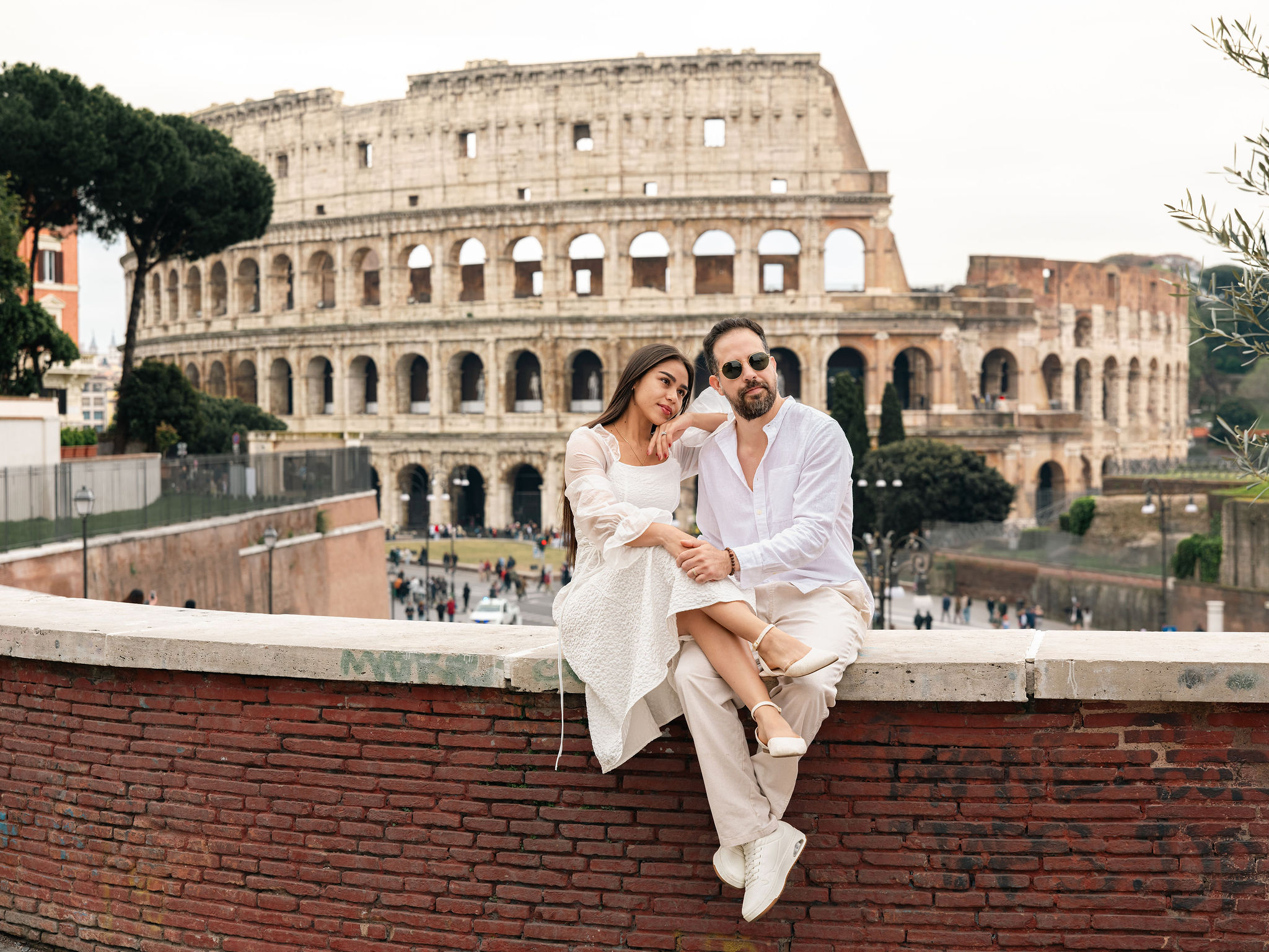 Woman in a flowing white dress at Belvedere Cederna, overlooking Via dei Fori Imperiali and the Vittoriano during sunset in Rome.