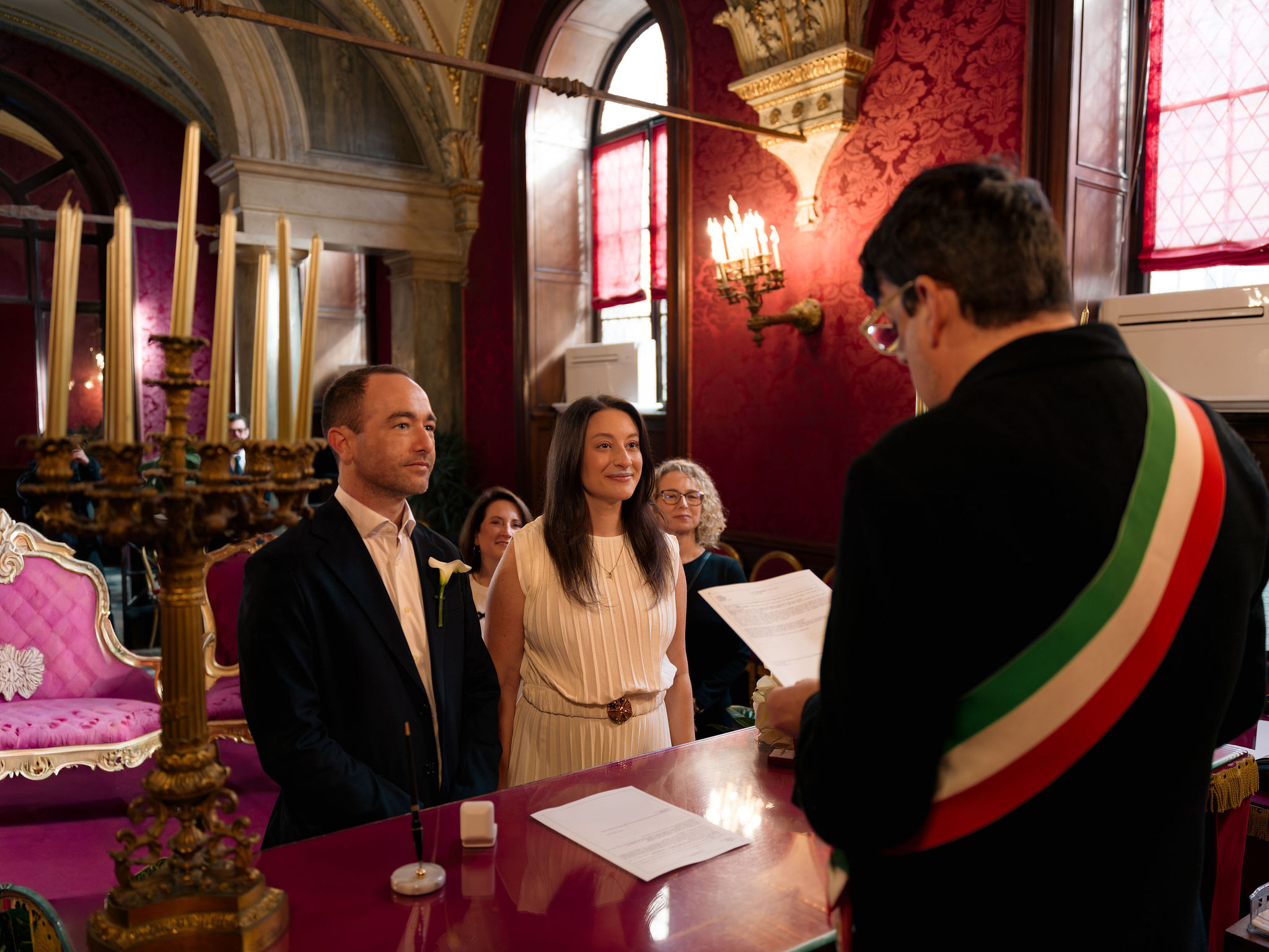 Couple standing before a civil officiant wearing the Italian tricolour sash in the Sala Rossa at the Campidoglio in Rome.
