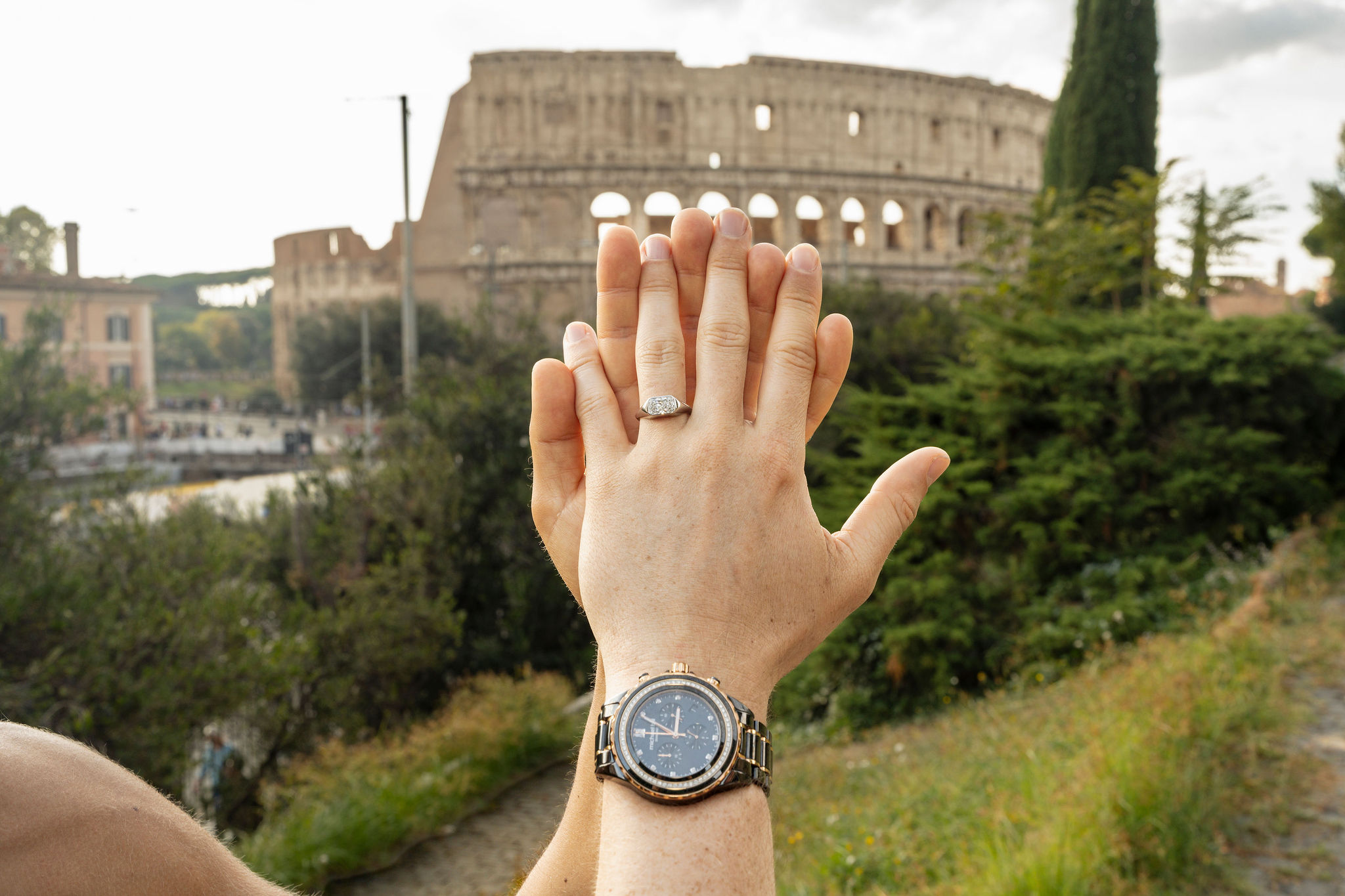 Close-up of a newly engaged couple showing an engagement ring, with the Colosseum softly blurred in the background.