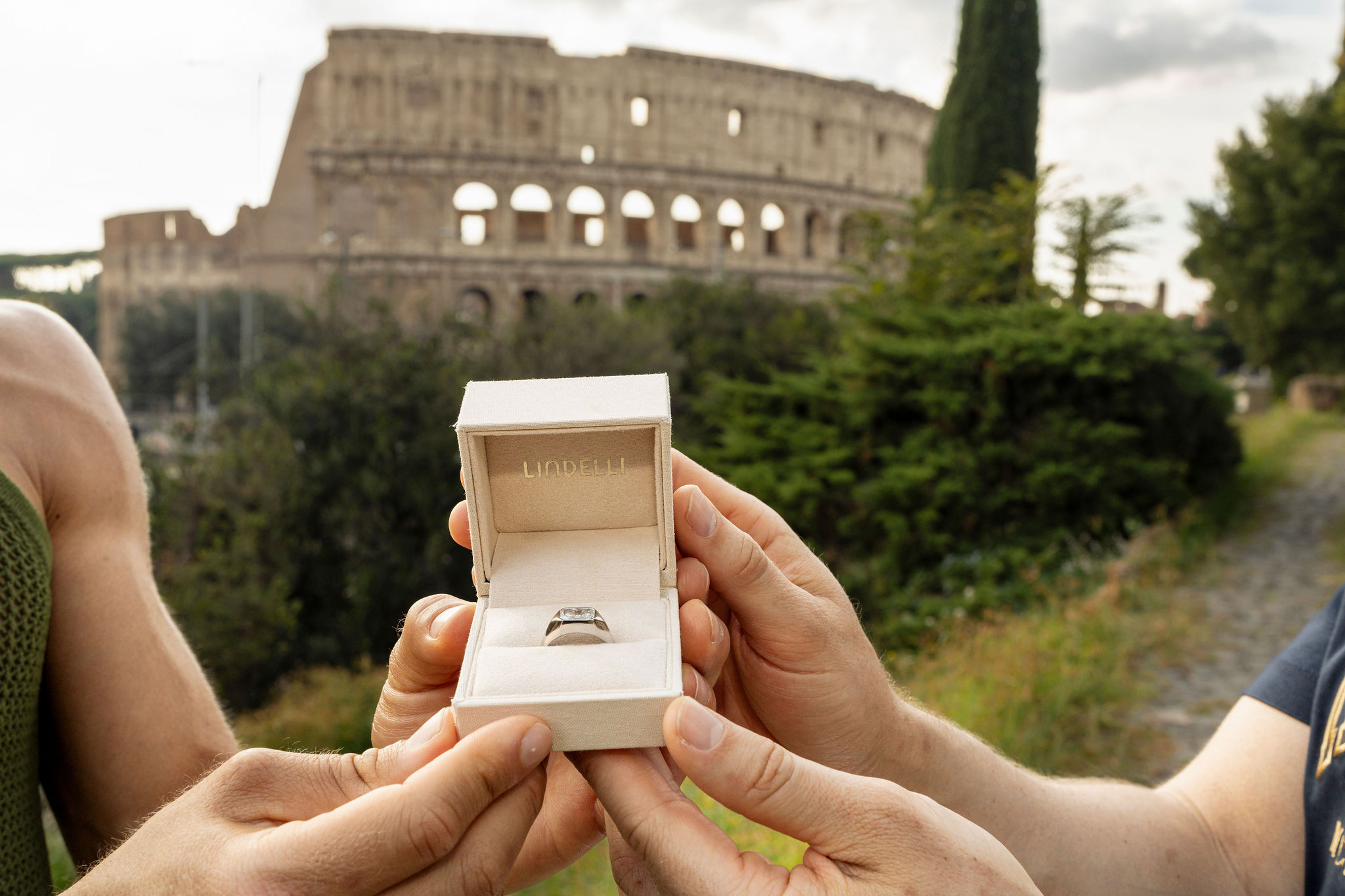 Two partners hold an open engagement ring box after their proposal, with the Colosseum in the background in Rome.