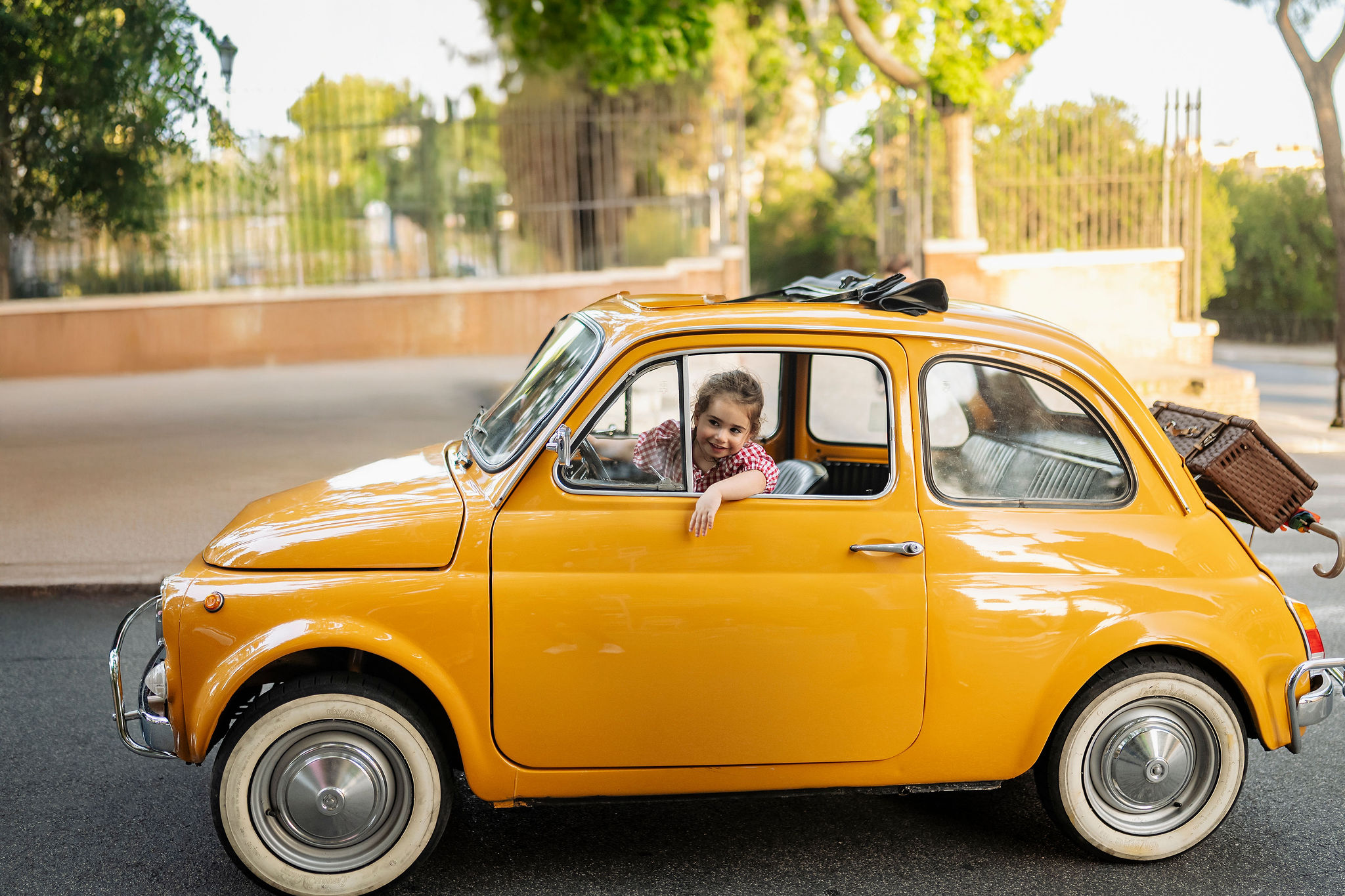 Young child smiling from the window of a vintage orange Fiat 500 during a family photoshoot in Rome.