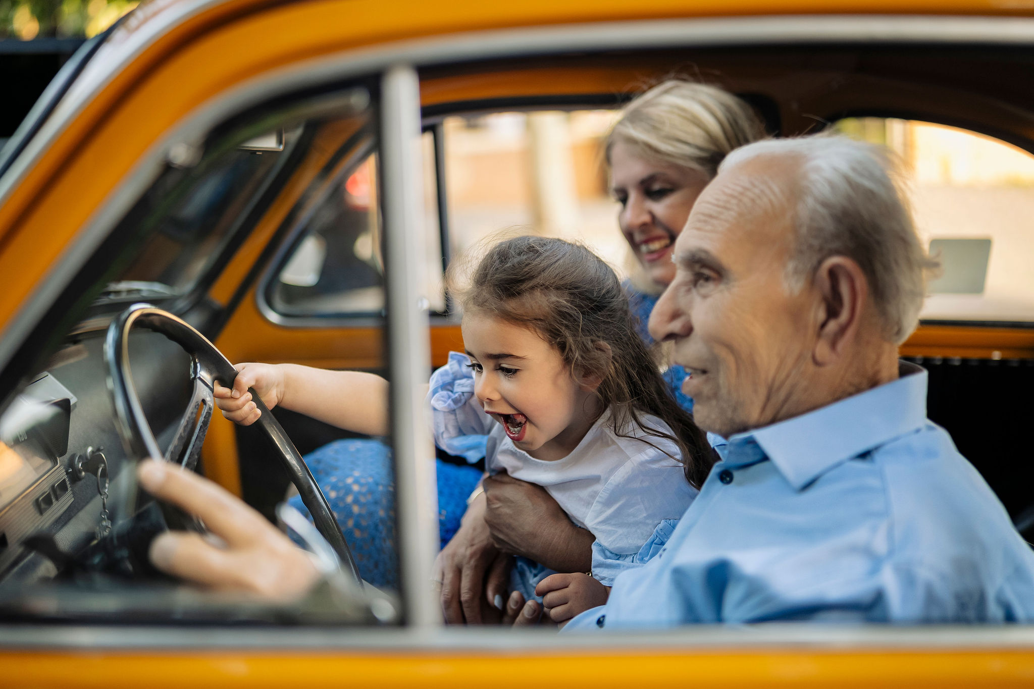 Grandfather and young granddaughter sharing a playful moment inside a vintage Fiat 500 during a multigenerational family photoshoot in Rome.