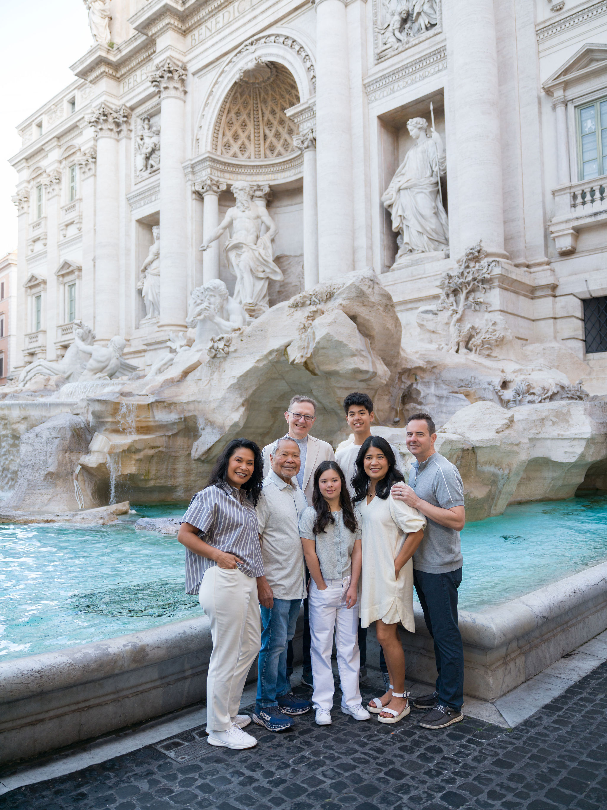 Multi-generational family smiling together in front of the Trevi Fountain during a family photoshoot in Rome.