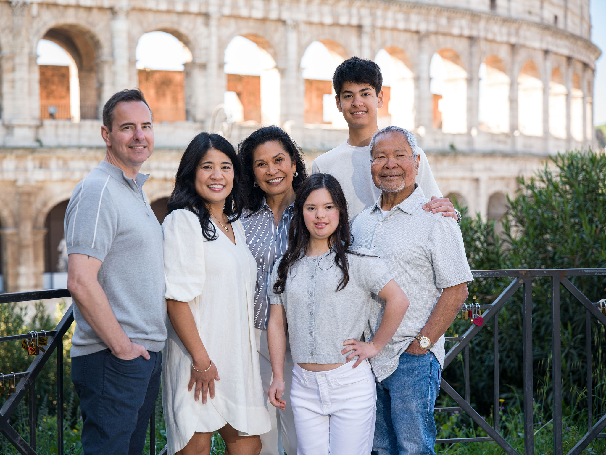 Multi-generational family portrait in Rome with parents, children, and grandparents smiling together in front of the Colosseum.