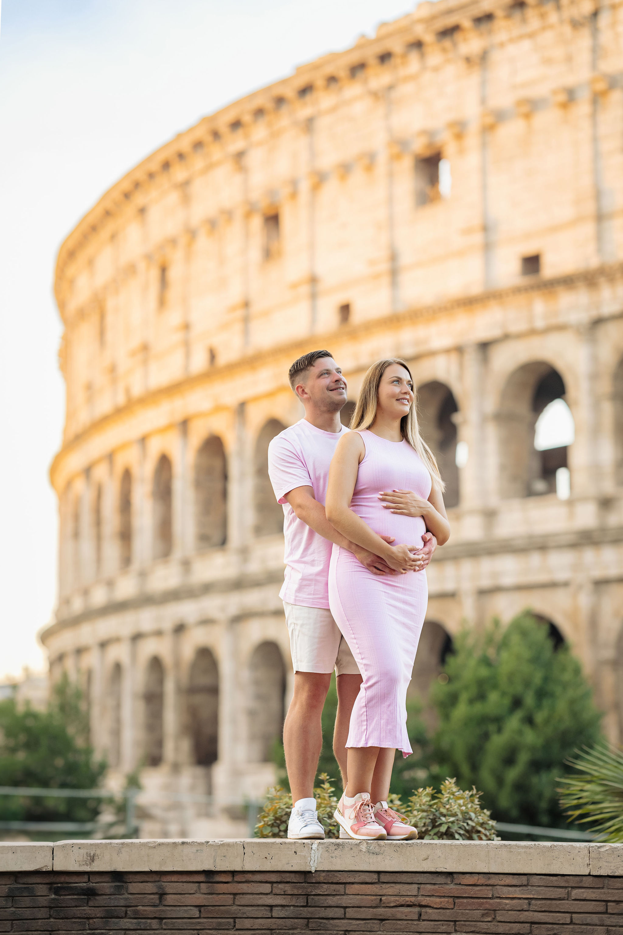     Expectant parents posing on a quiet street with the Colosseum behind them.