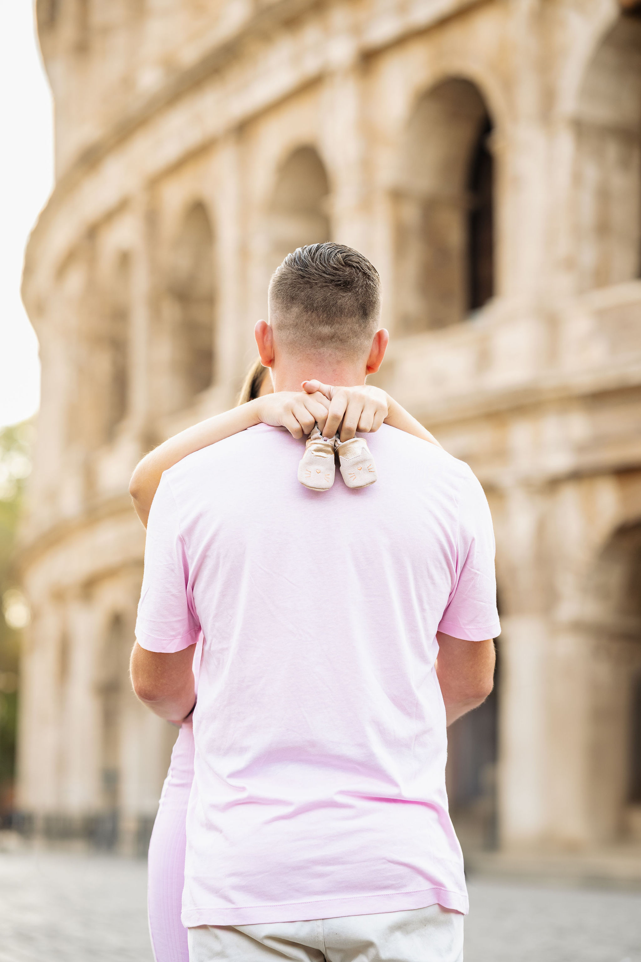     Expectant mother in a fitted pink dress posing comfortably with her partner in Rome.