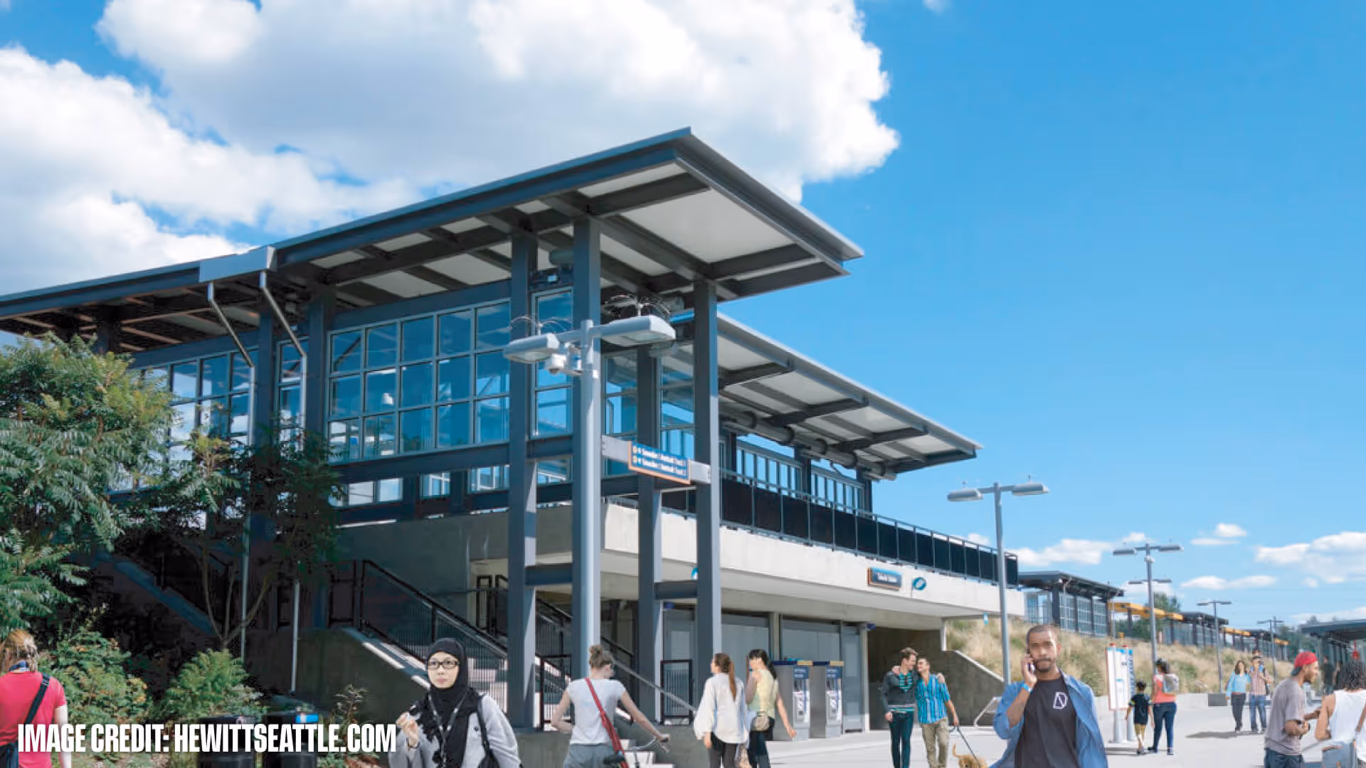 Modern public transit station with people walking and a man talking on a phone under a bright blue sky.
