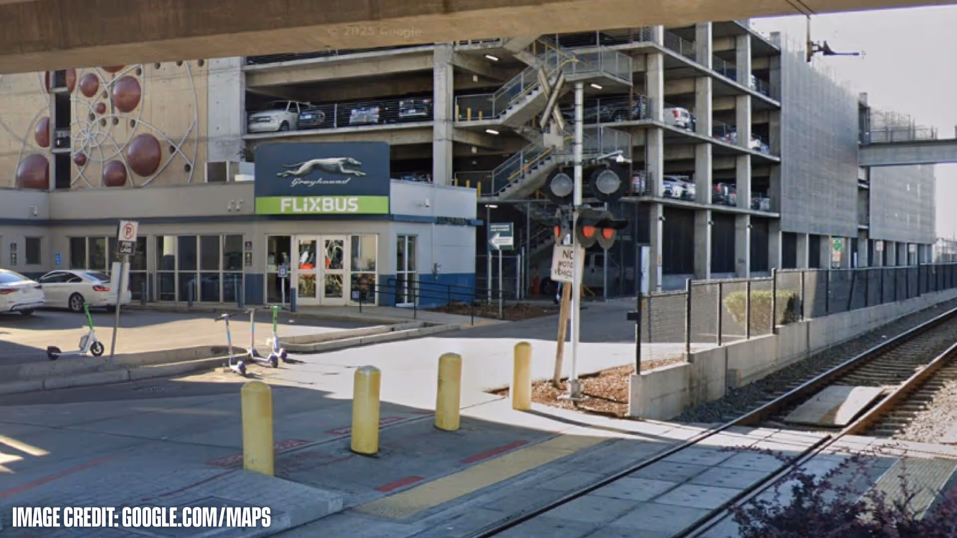 FlixBus station entrance next to a multi-level parking garage and railroad tracks crossing in front.
