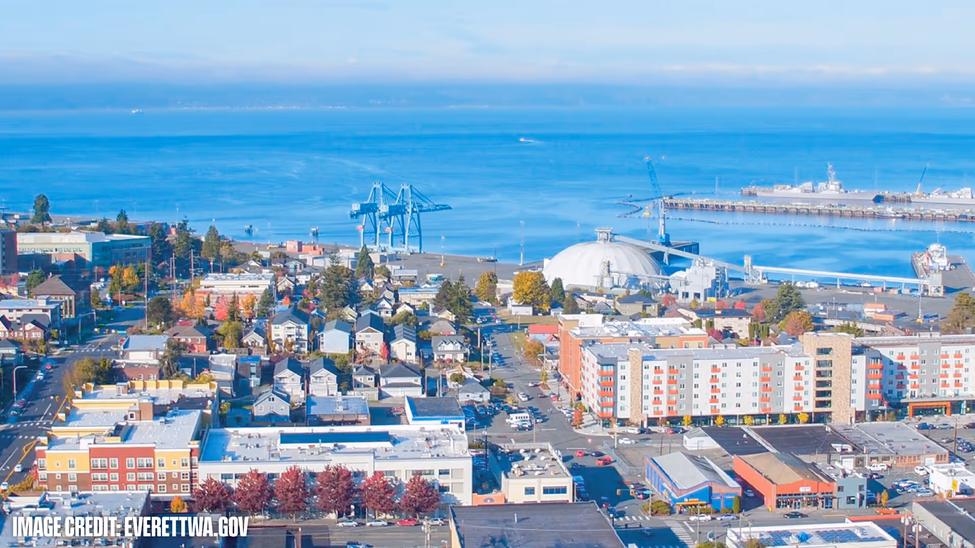 Aerial view of Everett cityscape with residential buildings, industrial port structures, and blue water in the background.