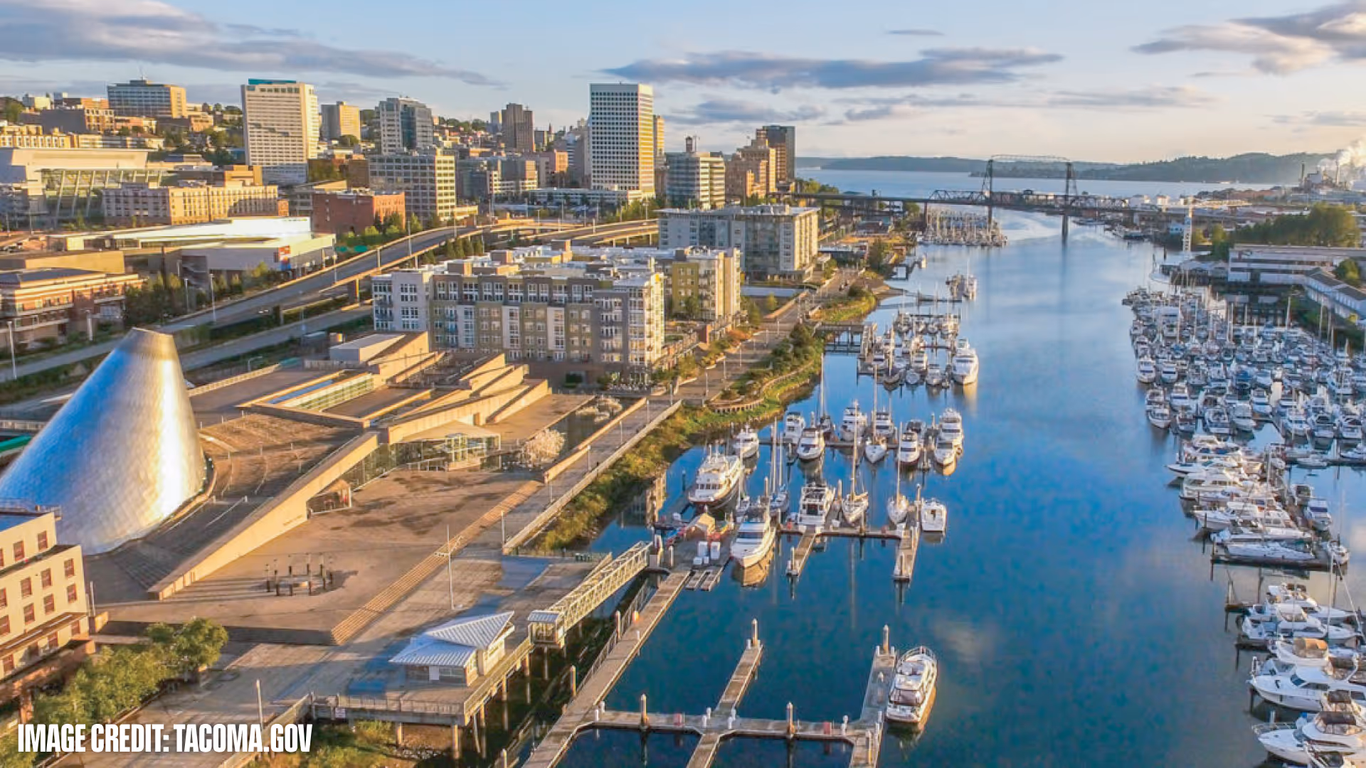 Aerial view of downtown Tacoma with marina full of boats, waterfront buildings, and a bridge over the water.
