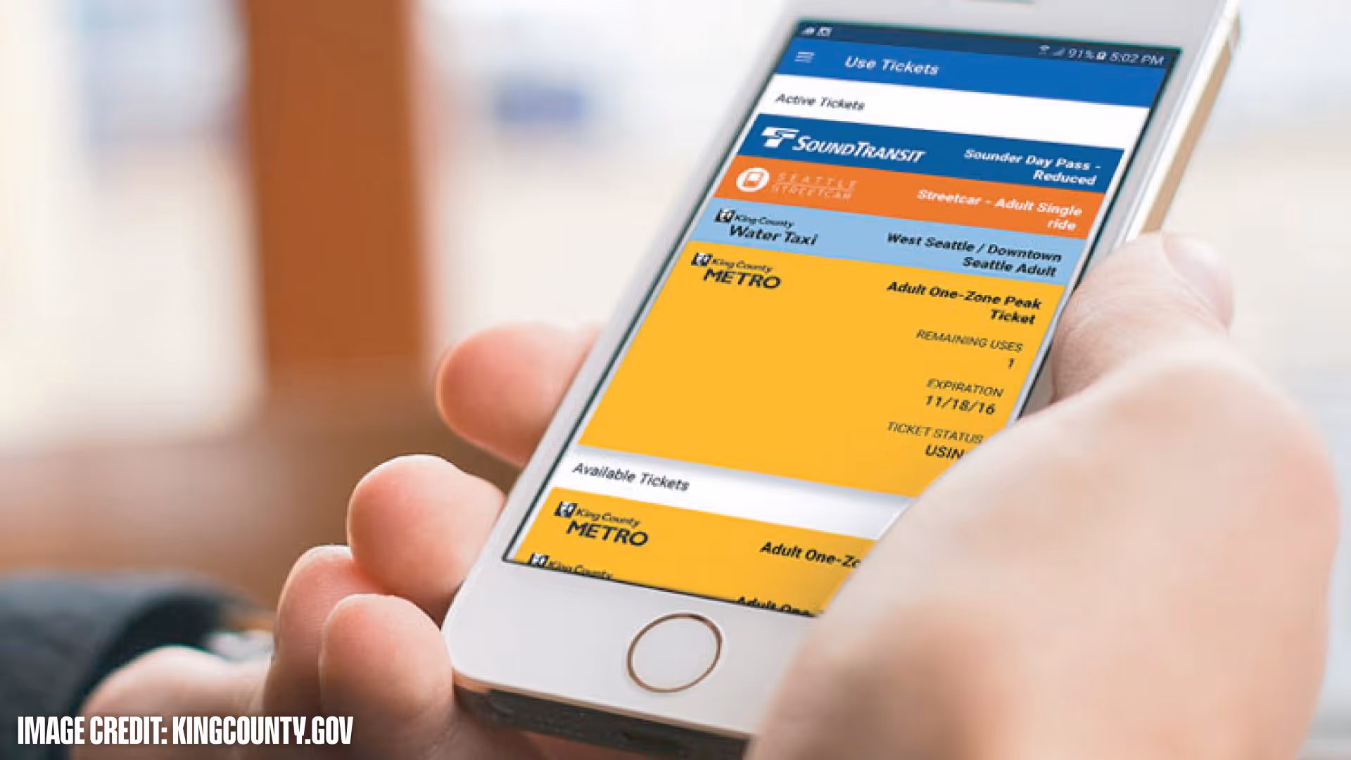 Hand holding a smartphone displaying a transit ticket app with active and available King County Metro and SoundTransit passes.