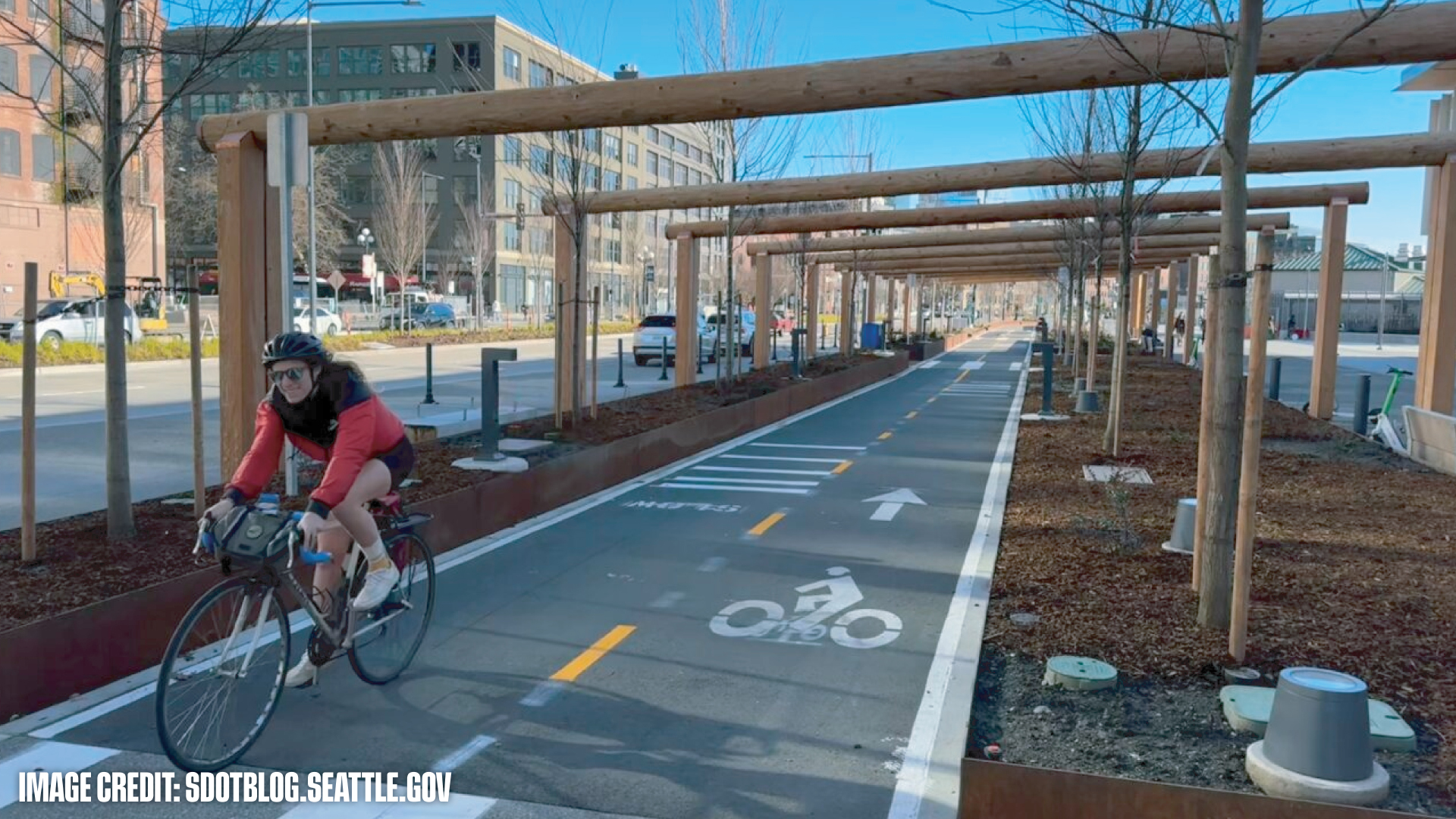 Cyclist wearing helmet riding on a dedicated bike lane under wooden pergolas in an urban area.