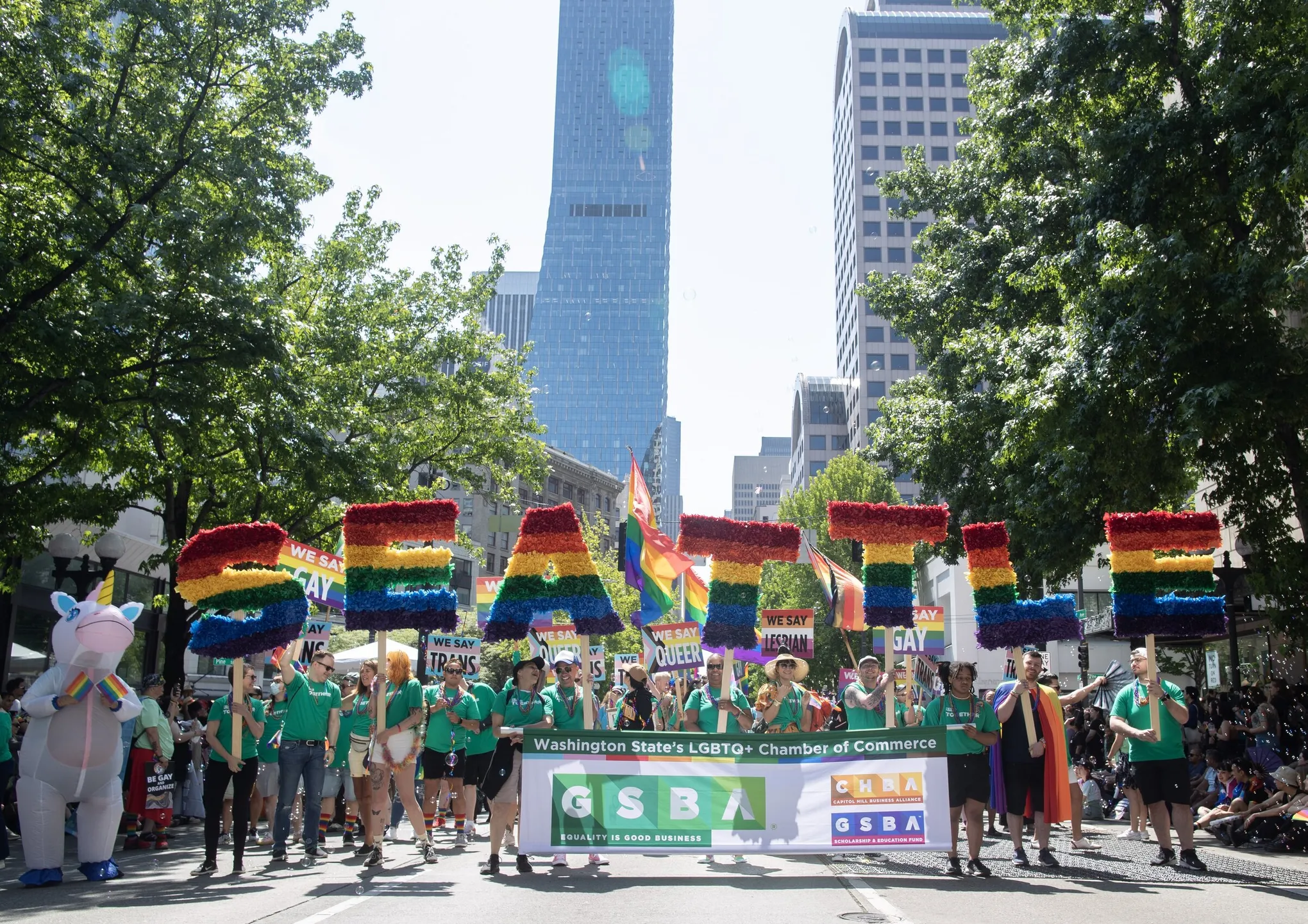 Group holding rainbow letters spelling SEATTLE and signs at Seattle Pride Parade in downtown.