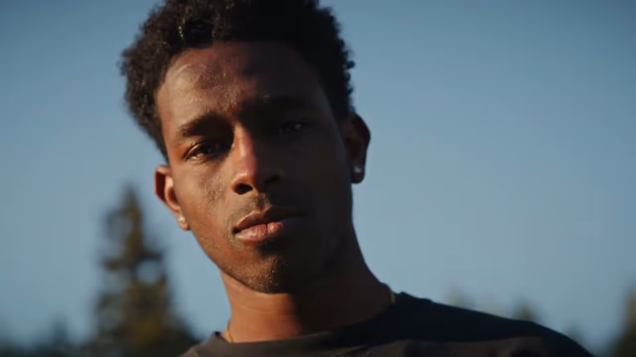 Portrait of a serious young Black man with short curly hair outdoors against a clear blue sky.