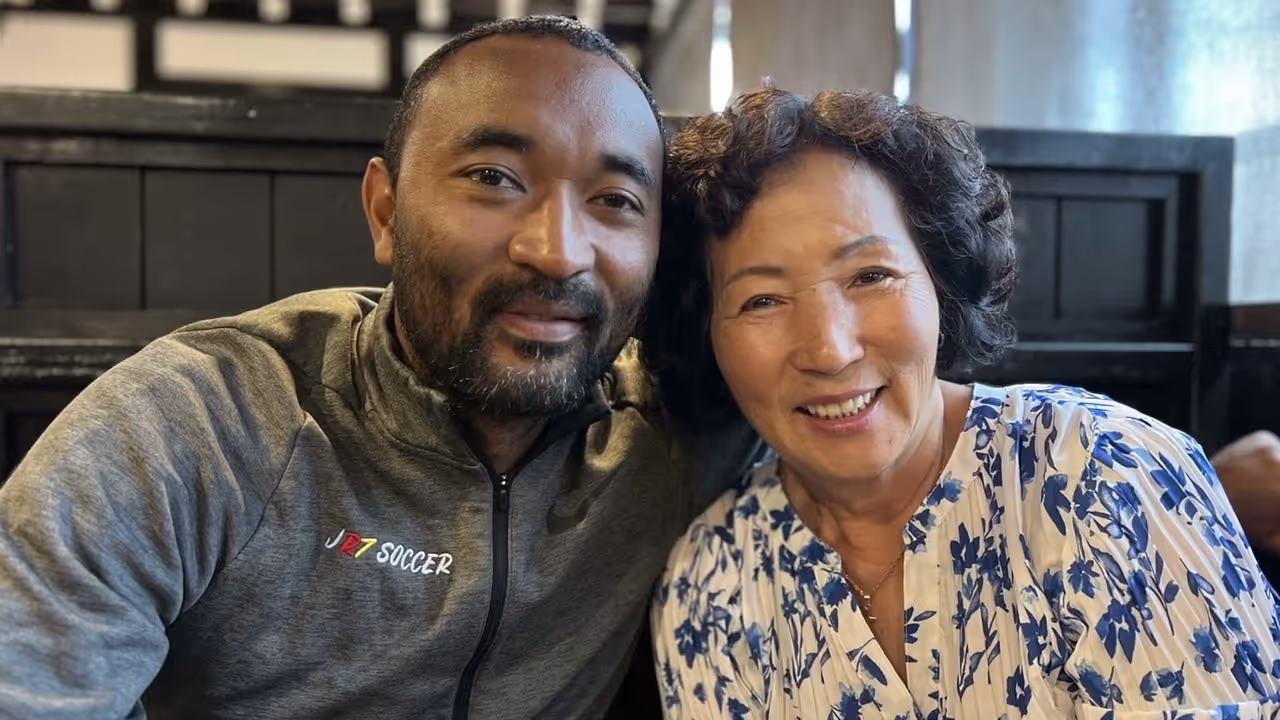 Smiling man in gray jacket with JR7 Soccer logo next to a woman wearing a white blouse with blue flowers.