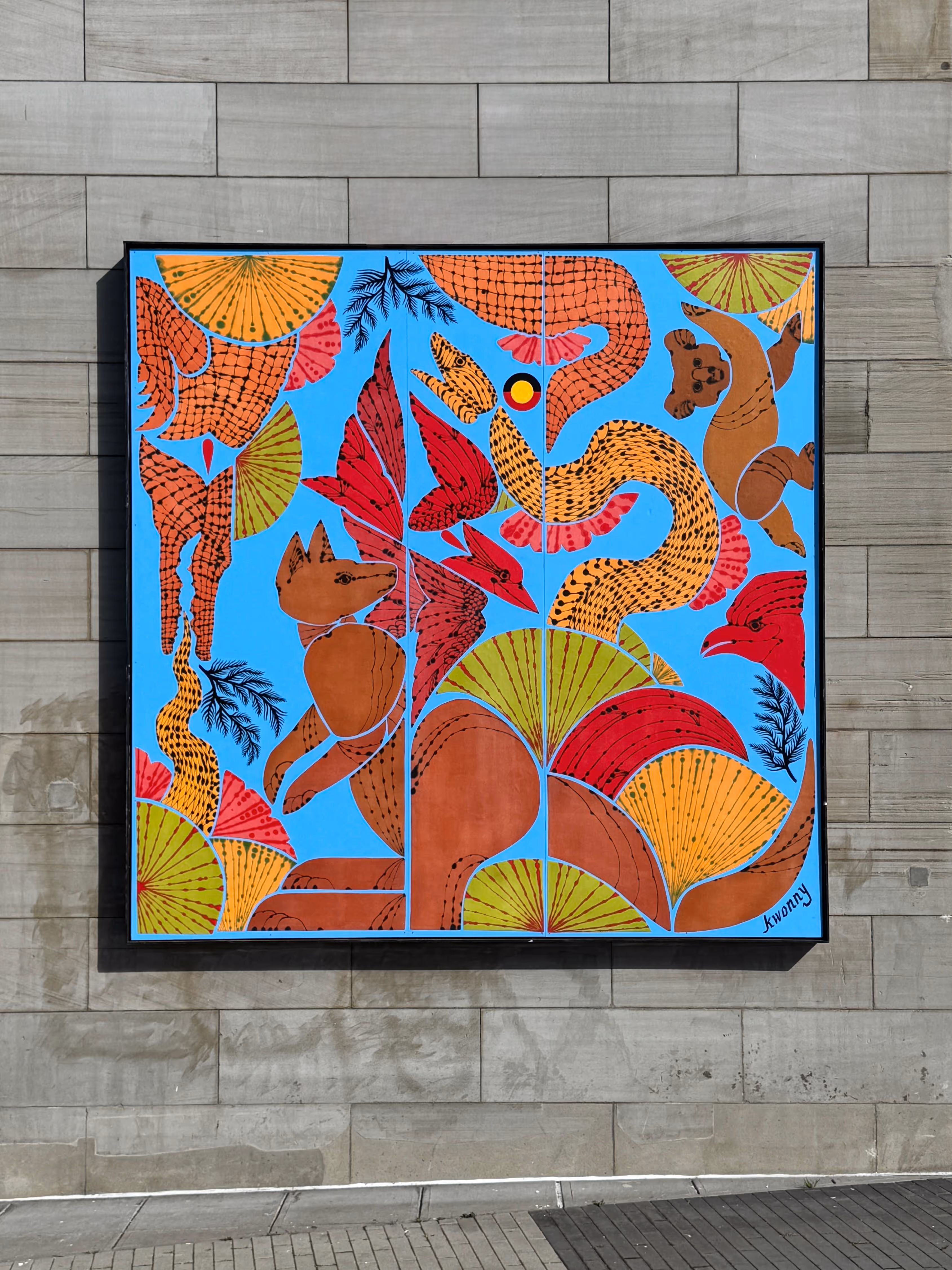 Colorful mural with stylized animals, birds, and plants on a bright blue background mounted on a wall.