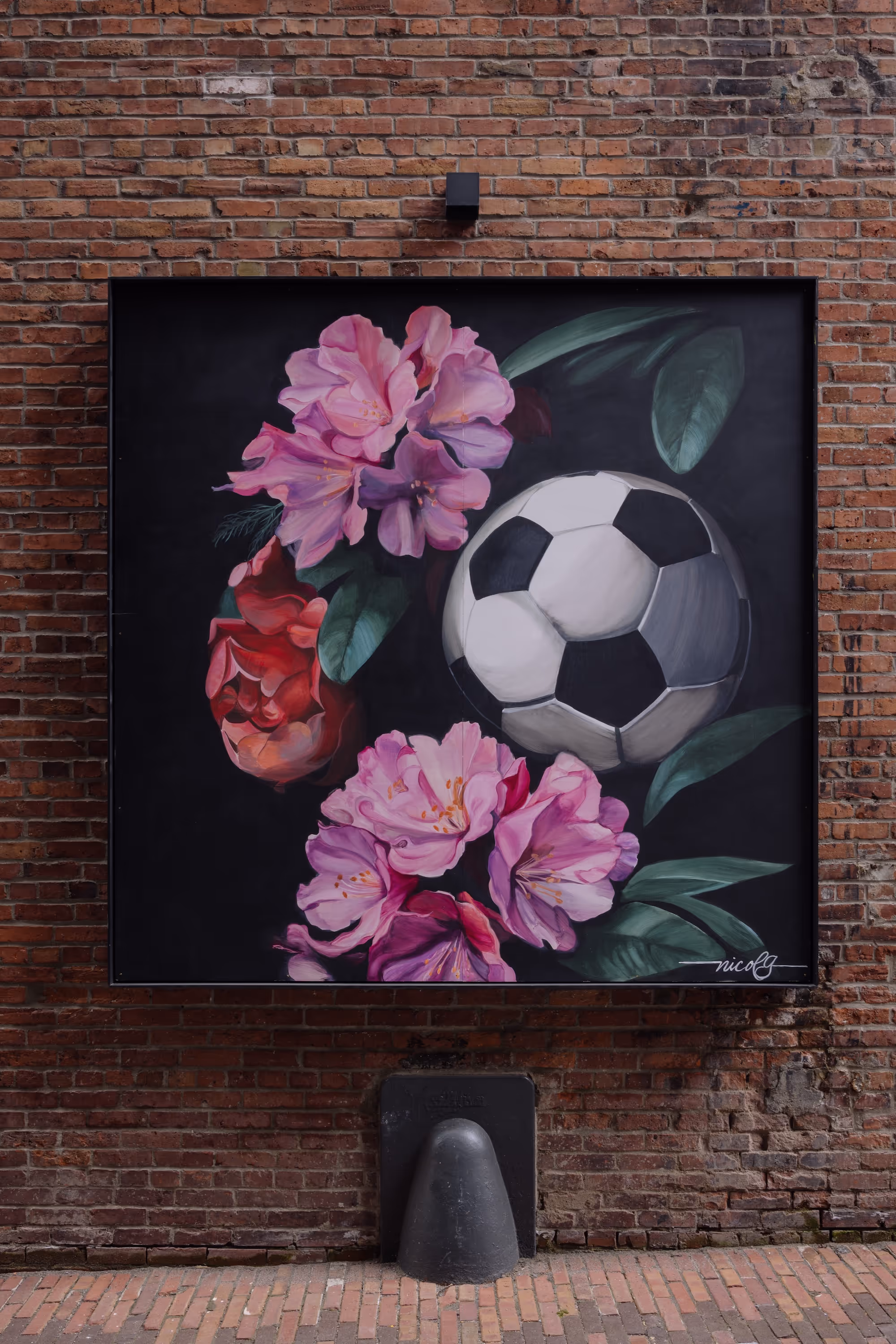 Mural on brick wall of a black and white soccer ball surrounded by pink and red flowers with green leaves.