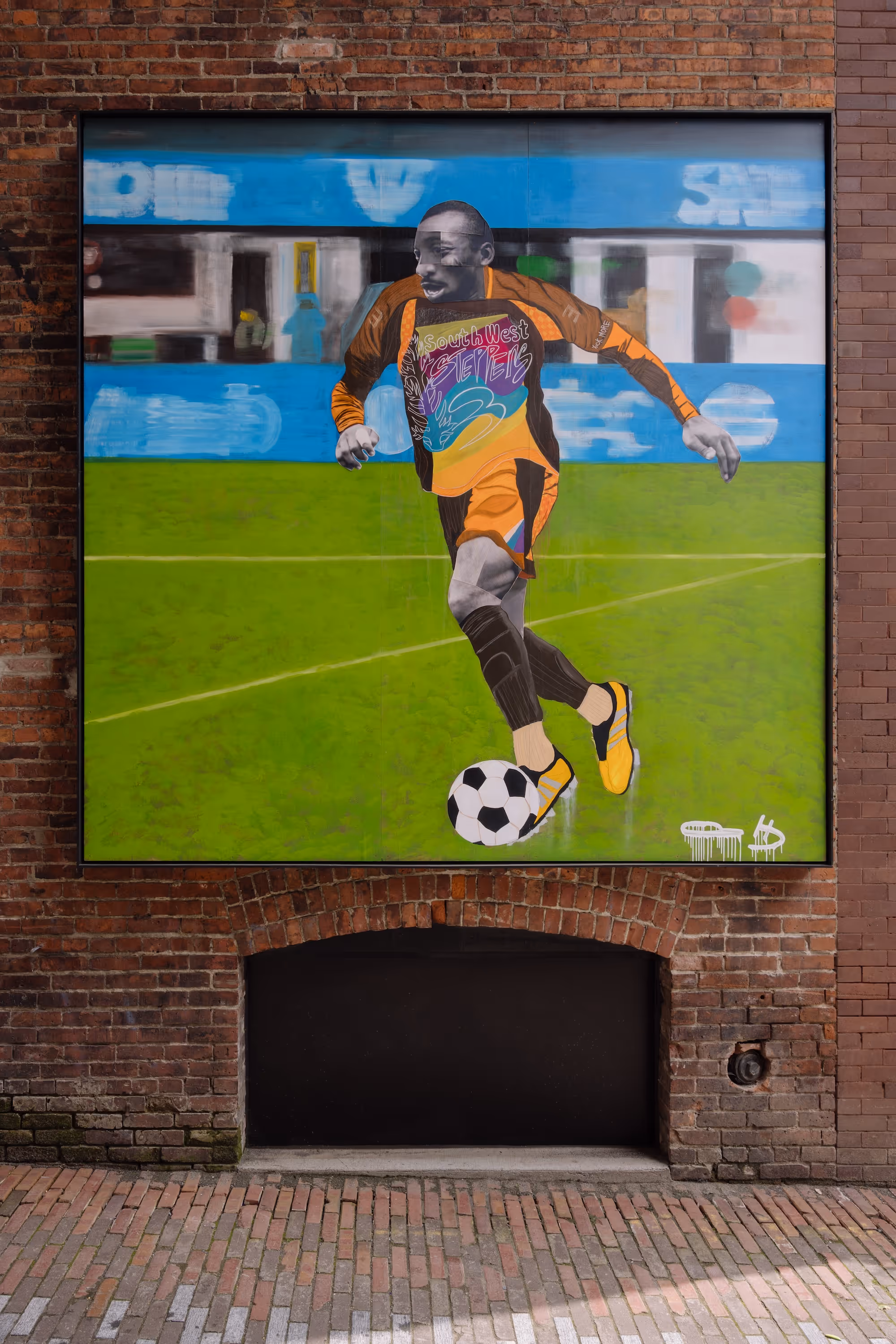 Wall mural of a soccer player in orange kit kicking a black and white soccer ball on green field.