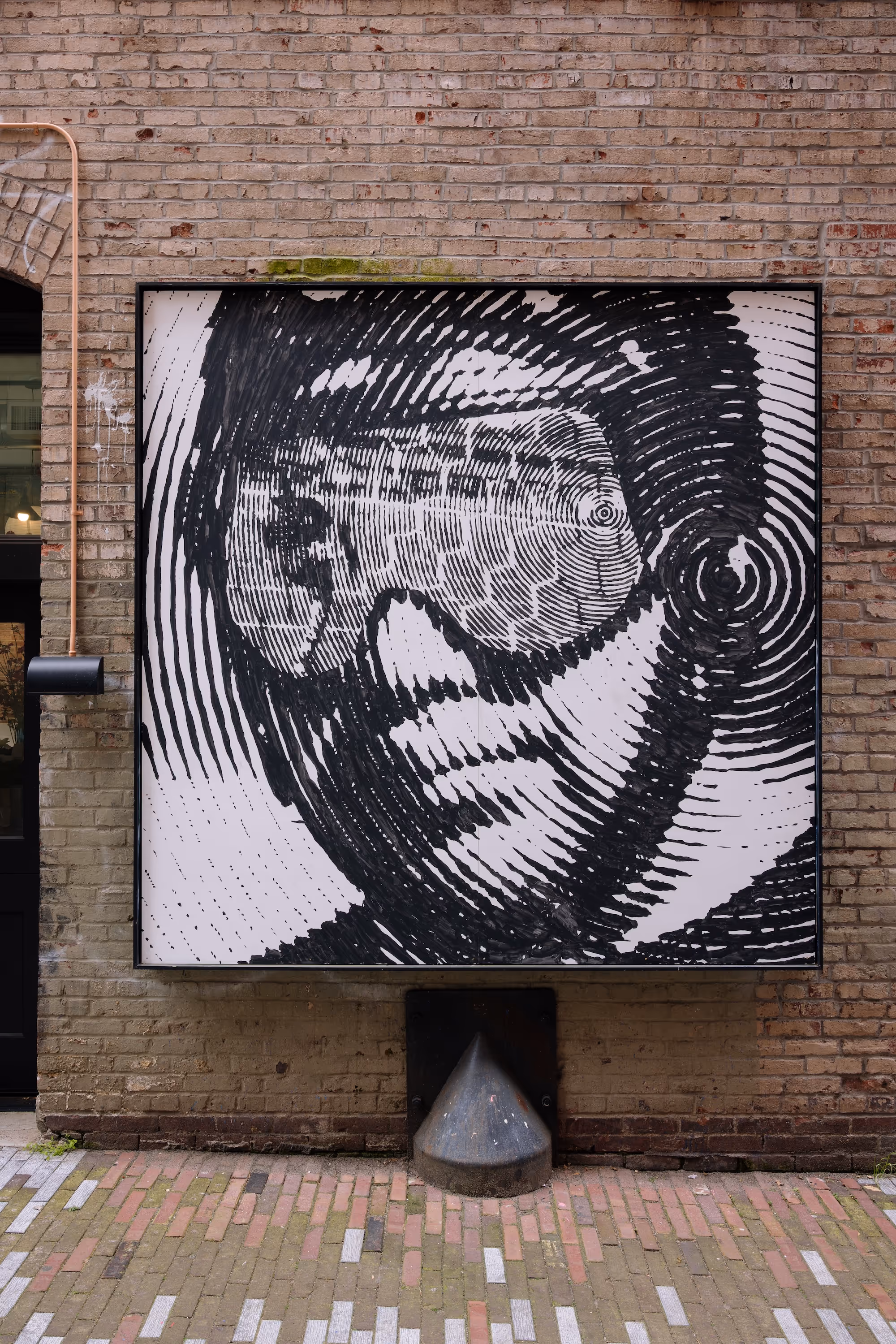 Black and white mural of a face wearing goggles made of concentric circular lines on a brick wall.