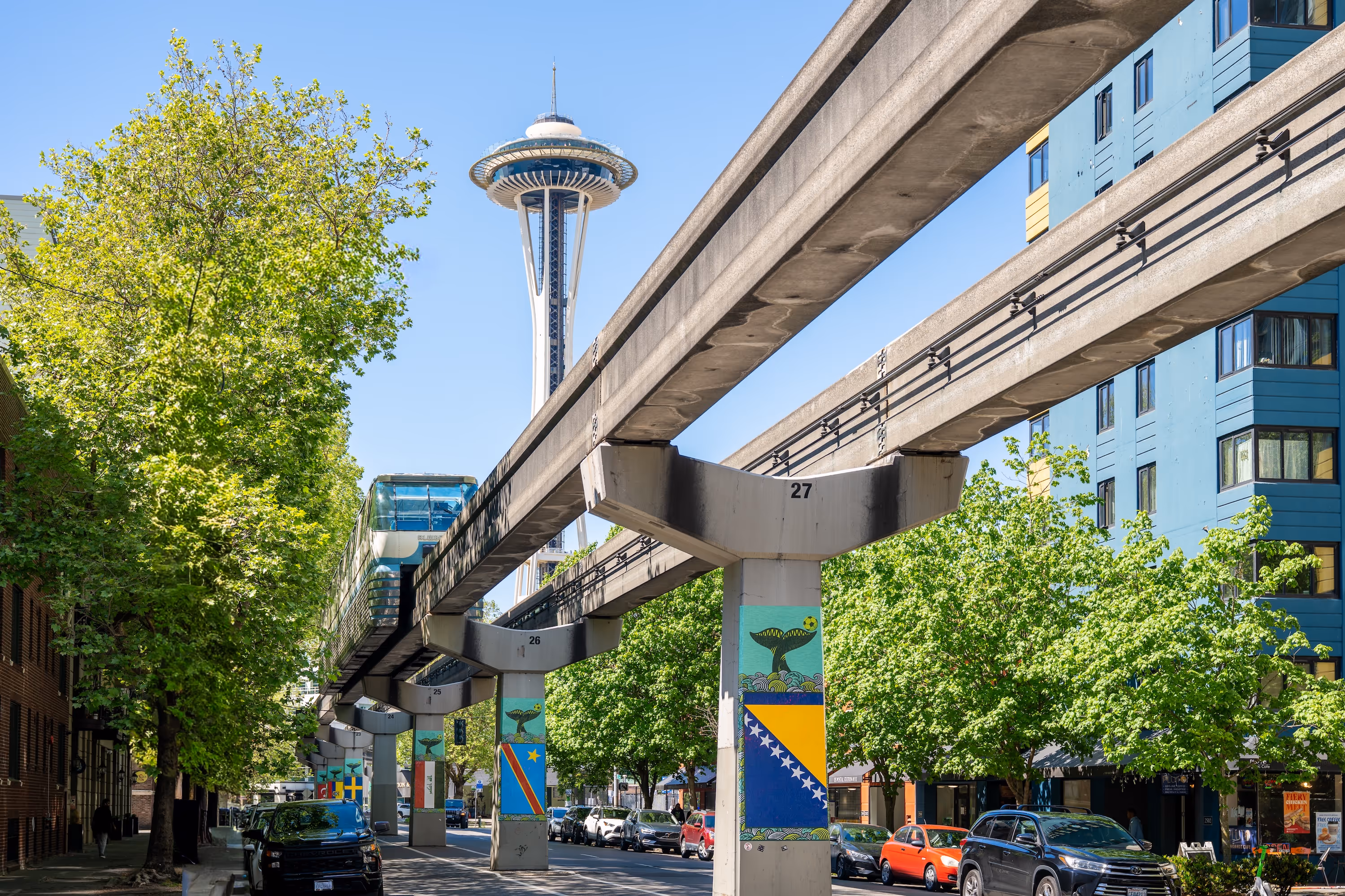 Seattle monorail track with flags on columns and Space Needle in the background on a sunny day.