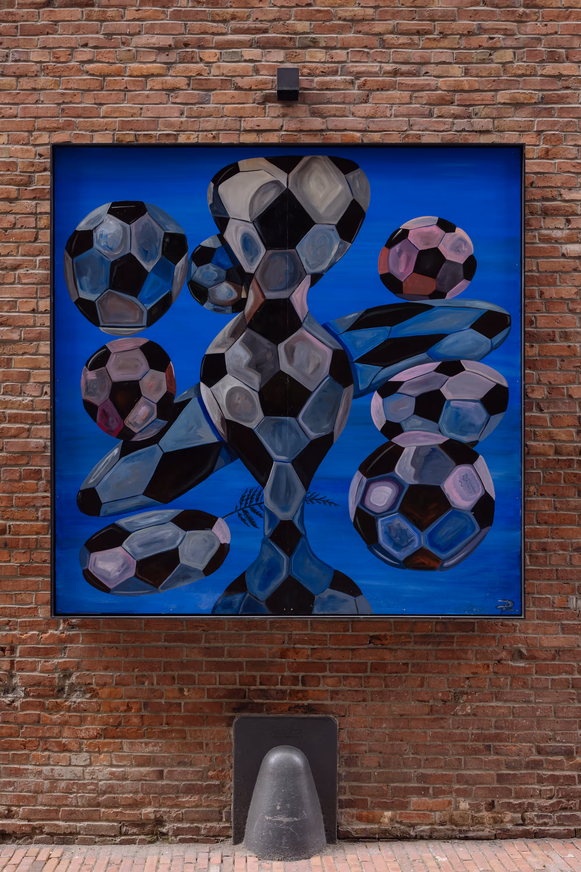 Abstract painting of distorted black and white soccer balls on a blue background mounted on brick wall.