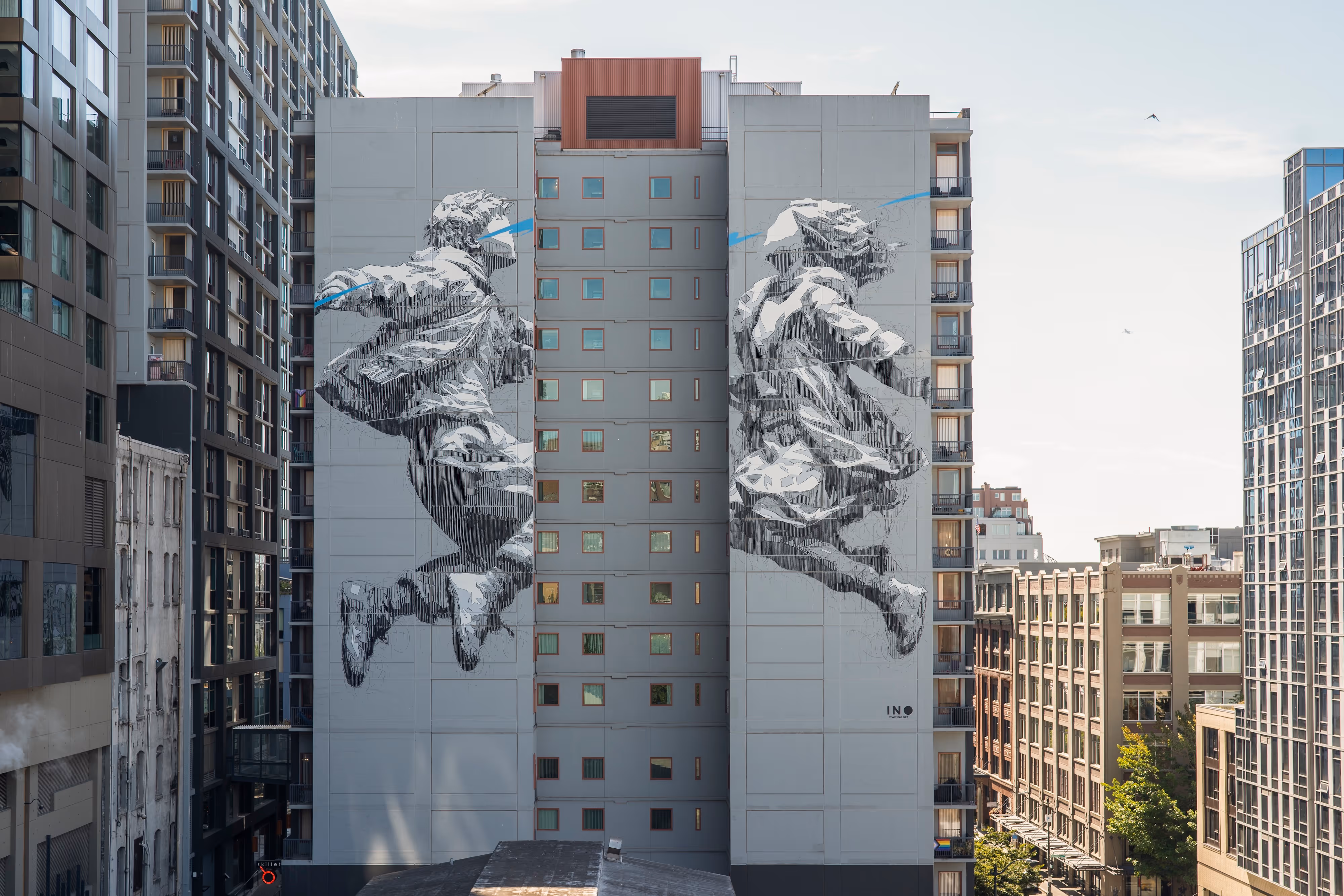 Large grayscale mural of two children jumping across two adjacent buildings in a cityscape.
