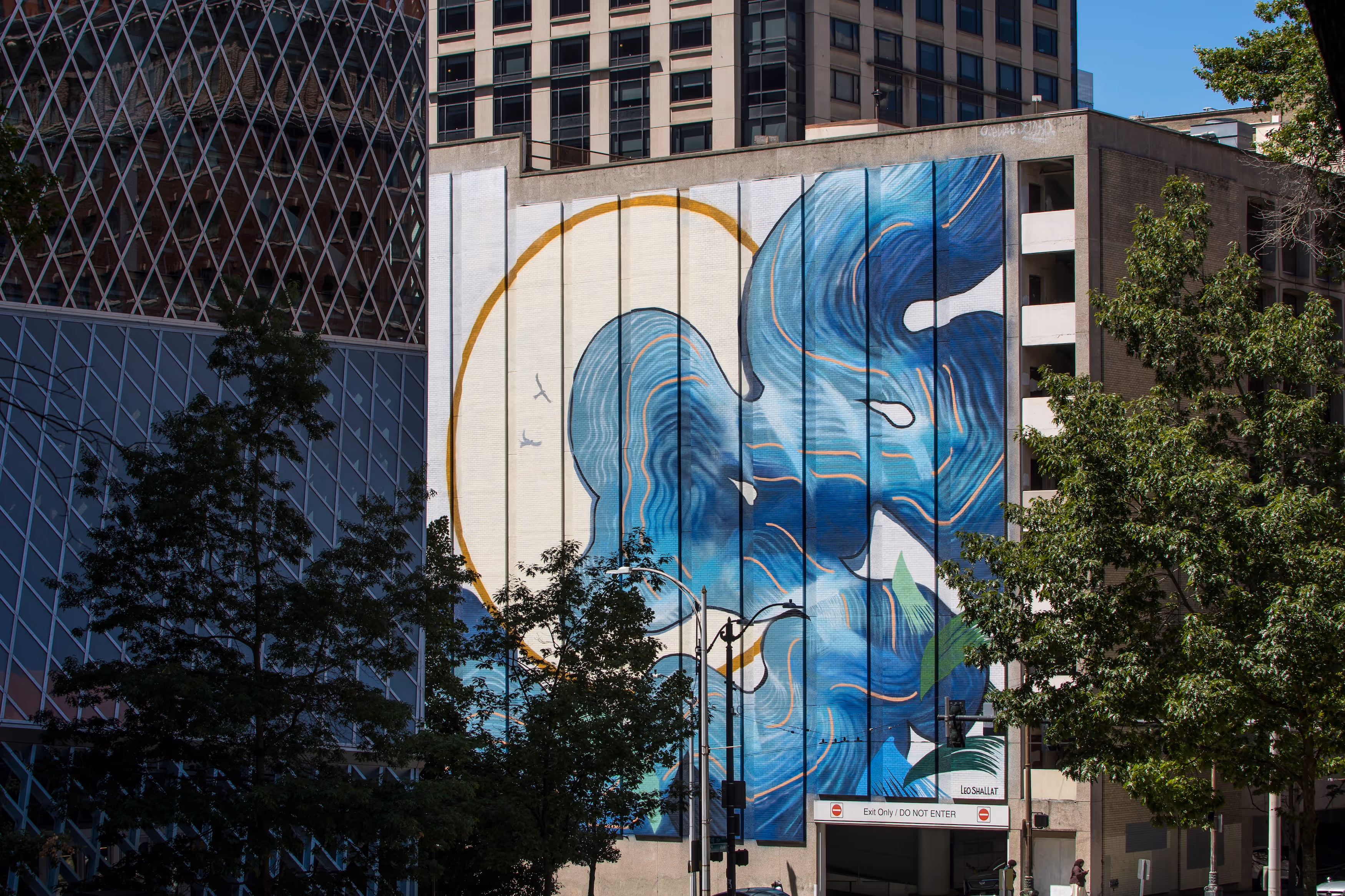 Large abstract mural with blue waves and a yellow circle on a tall building in a city street.