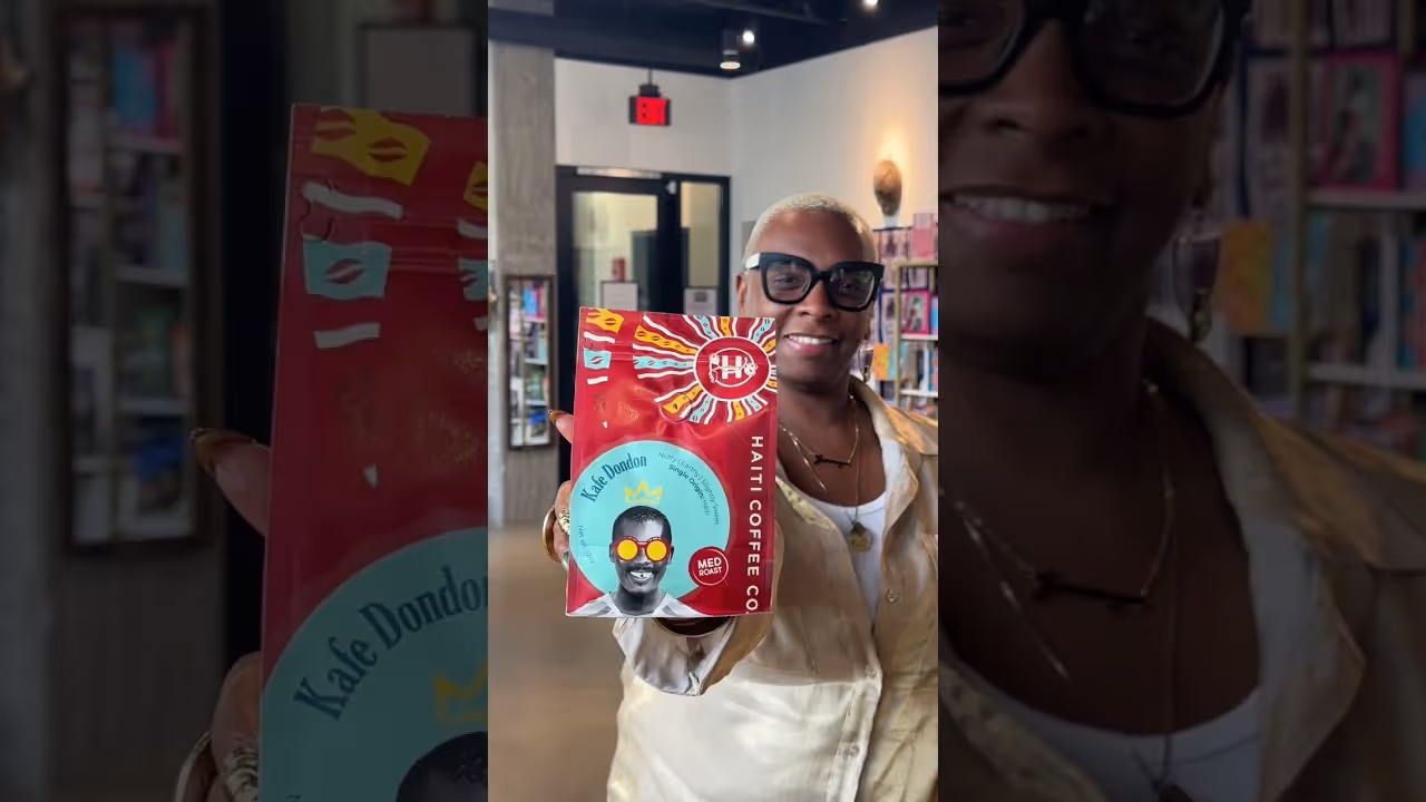 Person smiling and holding a red bag of Kafe Dondon medium roast Haiti Coffee Co. coffee.